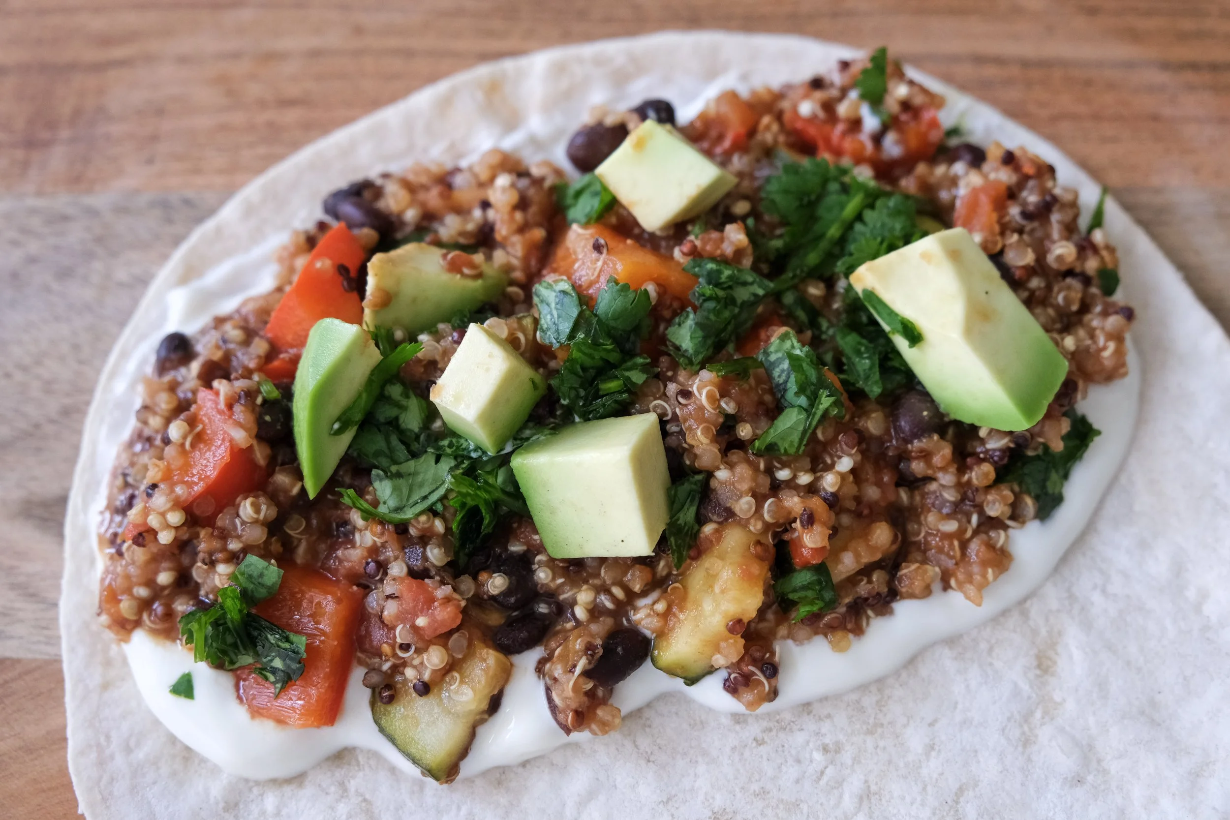 A warm flour tortilla spread with Greek yogurt, topped with Mexican quinoa, black beans, diced vegetables, coriander, and fresh avocado chunks.