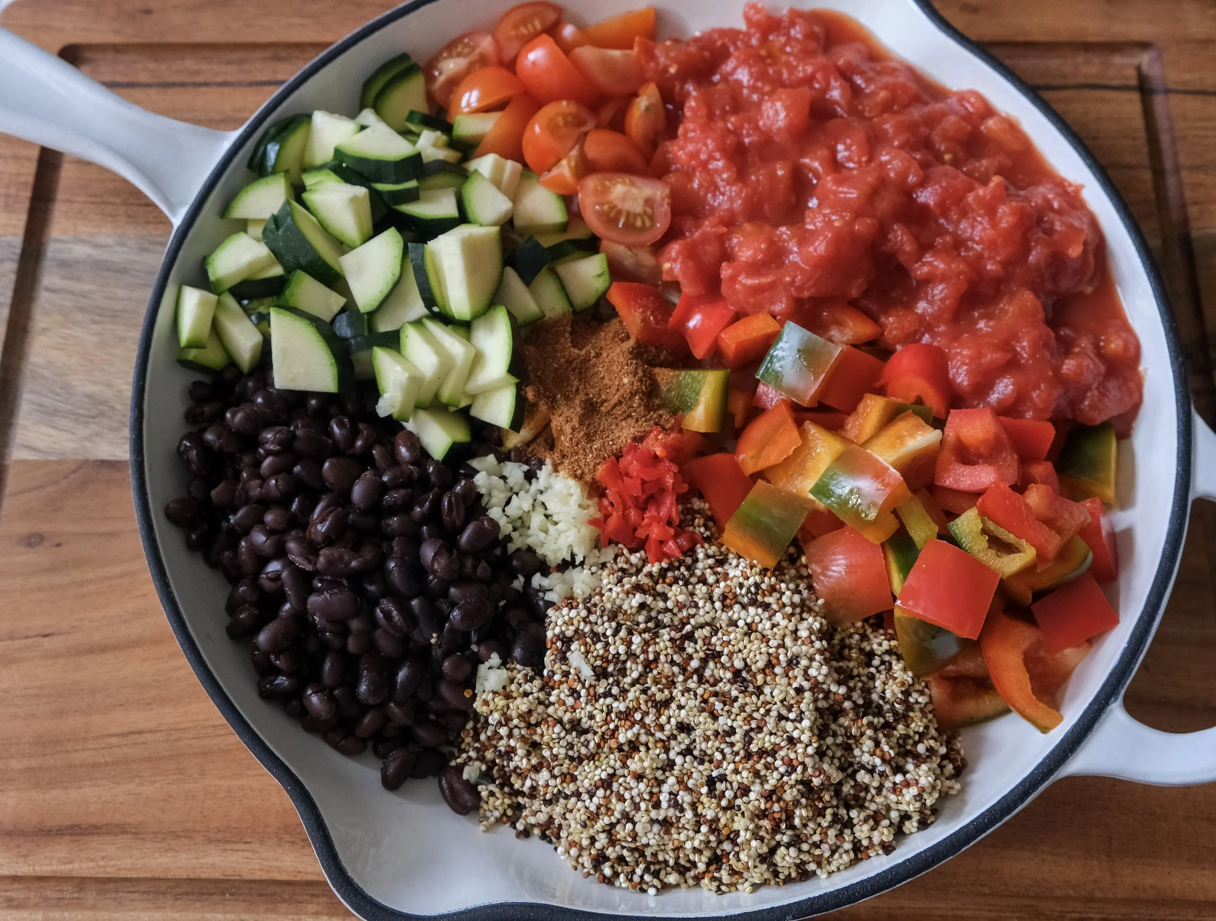 Uncooked ingredients for a one-pan Mexican quinoa and black bean bowl prepped inside a skillet.
