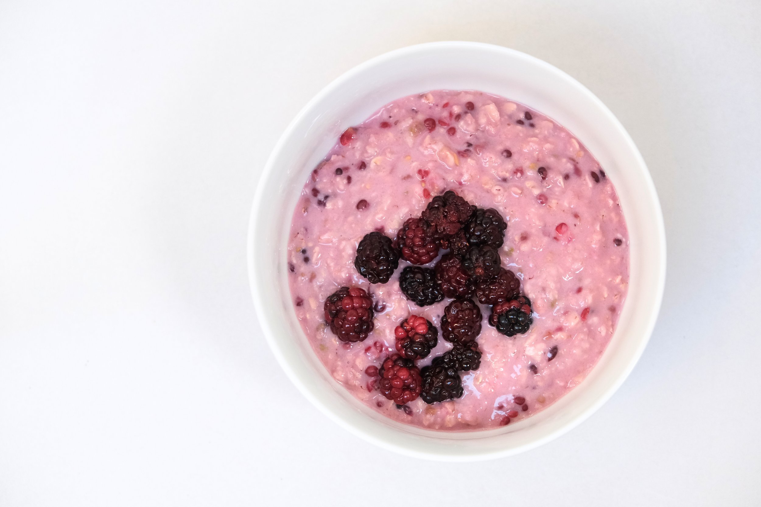 A top-down view of creamy pink high-fibre porridge topped with fresh whole blackberries in a white ceramic bowl.