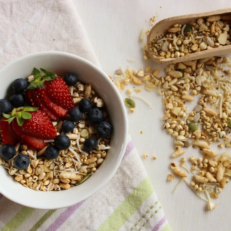 A bowl of homemade low FODMAP toasted muesli topped with fresh strawberries and blueberries, served on a striped linen napkin.
