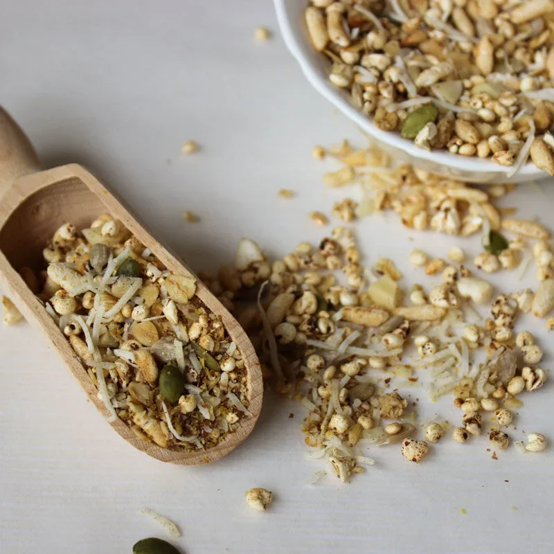 Hand-toasted low FODMAP muesli with puffed grains, pepitas, and shredded coconut in a wooden scoop and white bowl