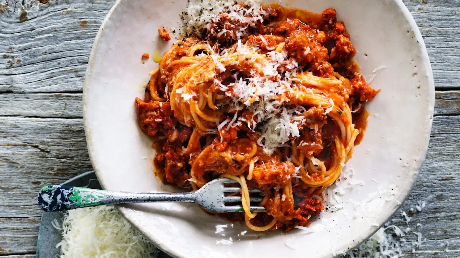 A bowl of spaghetti swirled with a rich, tomato-based white fish ragù and topped with freshly grated Parmesan cheese.