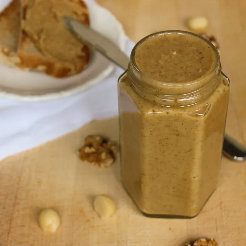 Creamy homemade macadamia walnut and maple nut butter in a glass jar with toast in the background