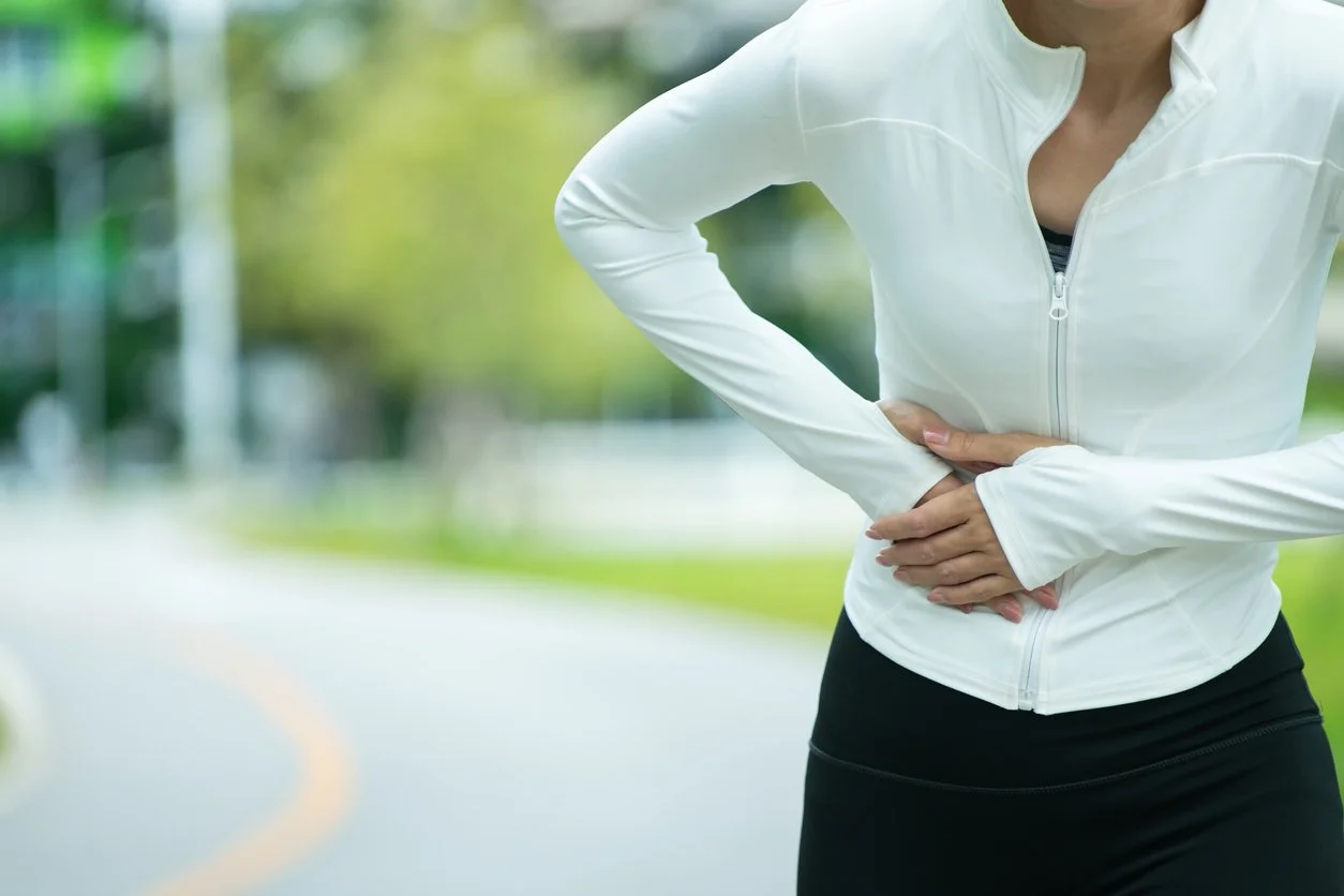 A female runner holding her stomach in pain on a running track, demonstrating symptoms of runner's gut and abdominal cramping.