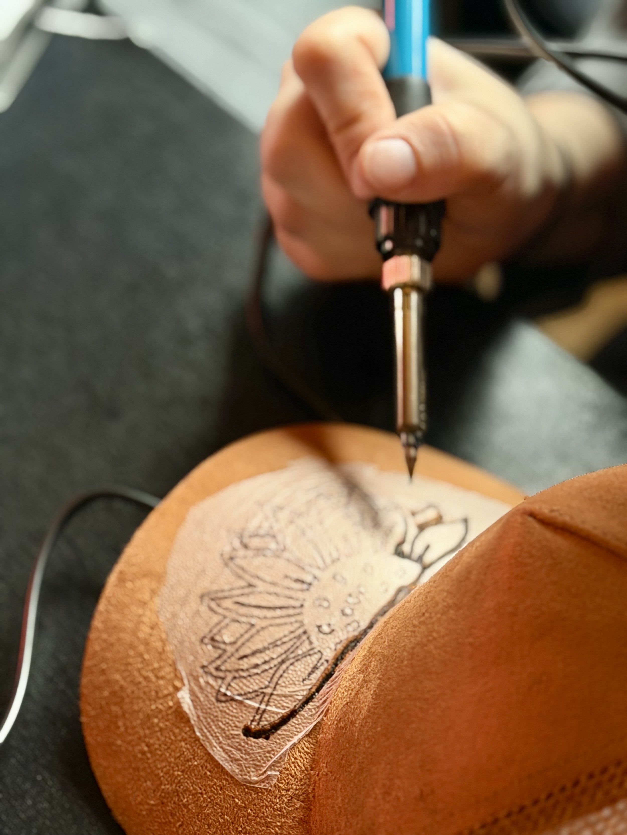 Close-up of a person sewing a leather shoe with a needle and blue thread.