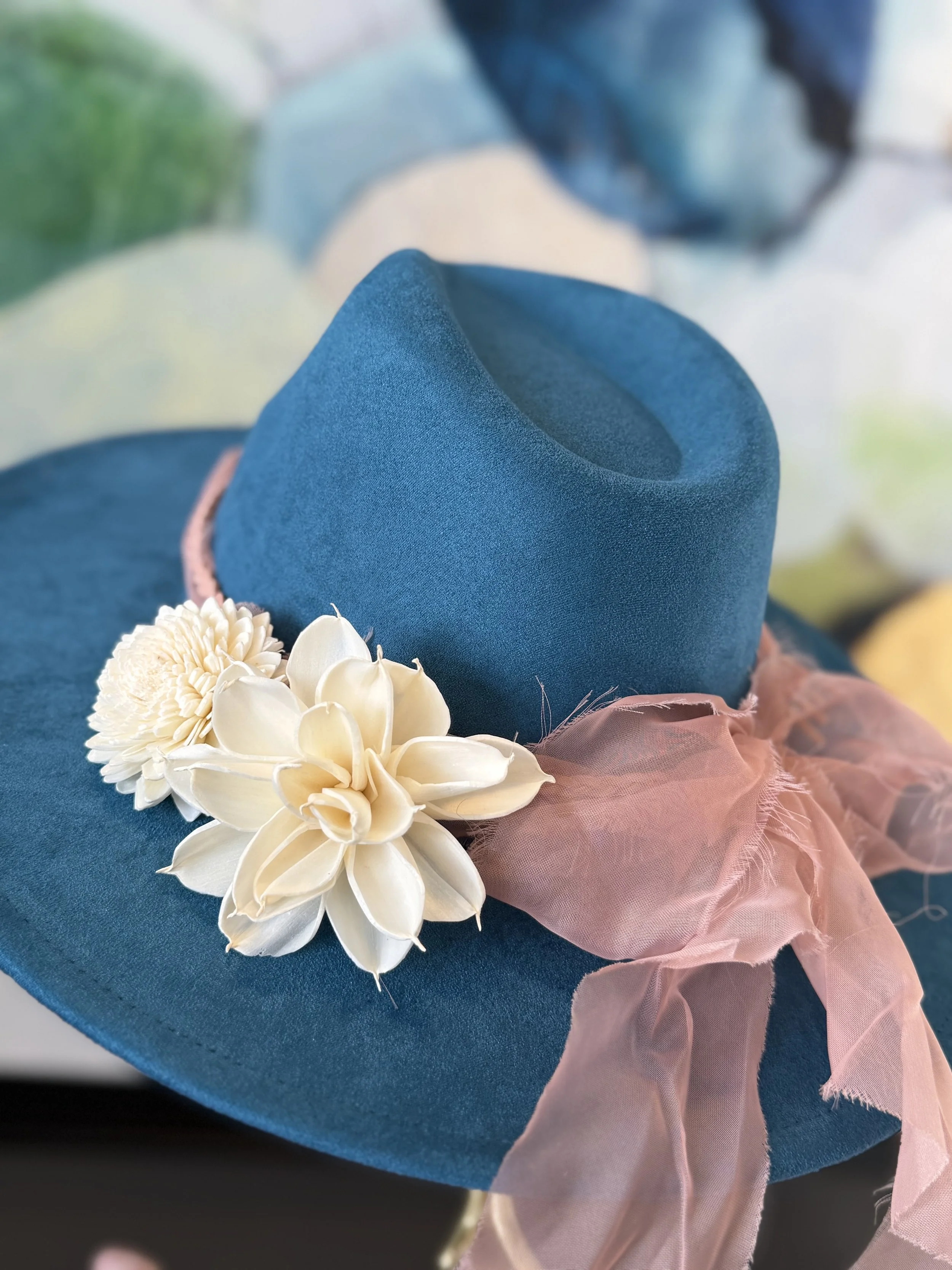 Close-up of a dark blue hat decorated with cream-colored flowers and a pink tulle ribbon.