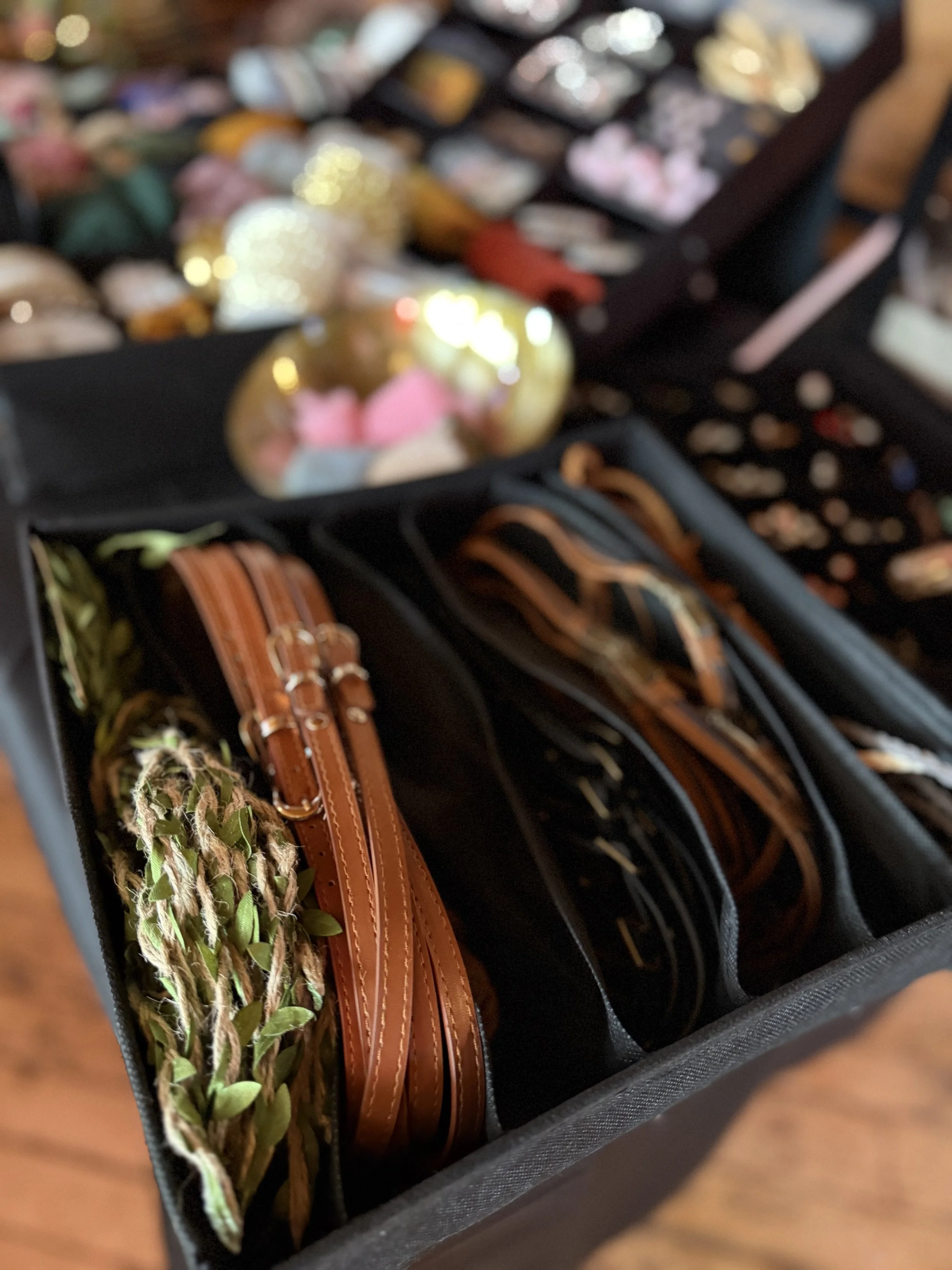 A black storage container with various jewelry items, including leather belts, bracelets, and a floral braided bracelet.