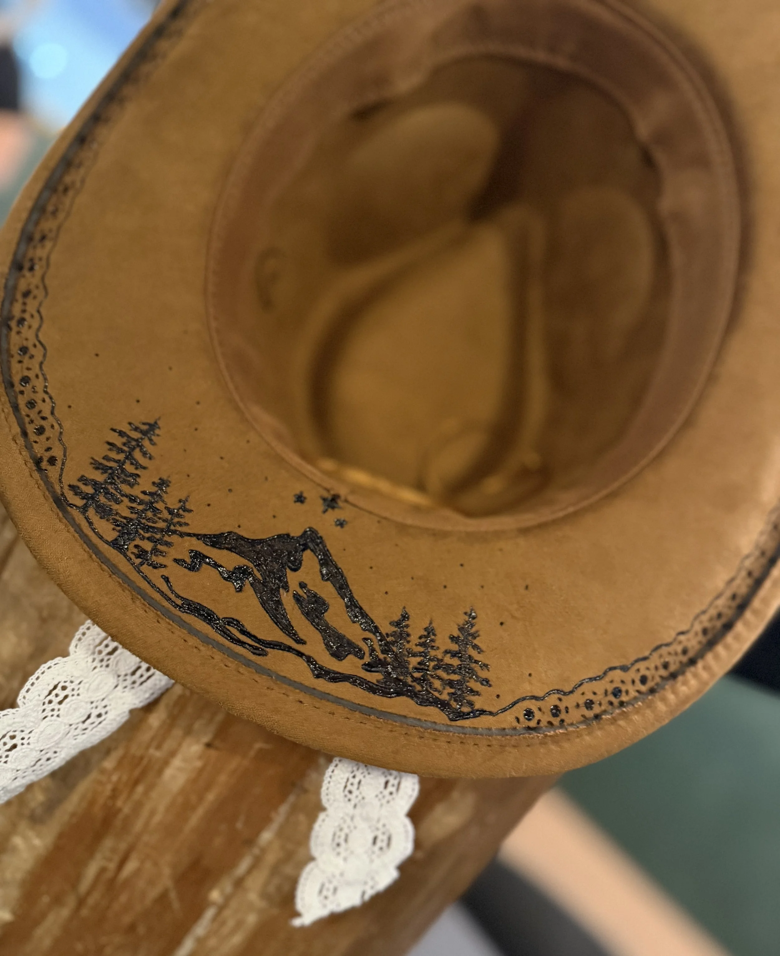 Close-up of a wooden surface with engraved mountain and forest designs, accented with a strip of white lace.