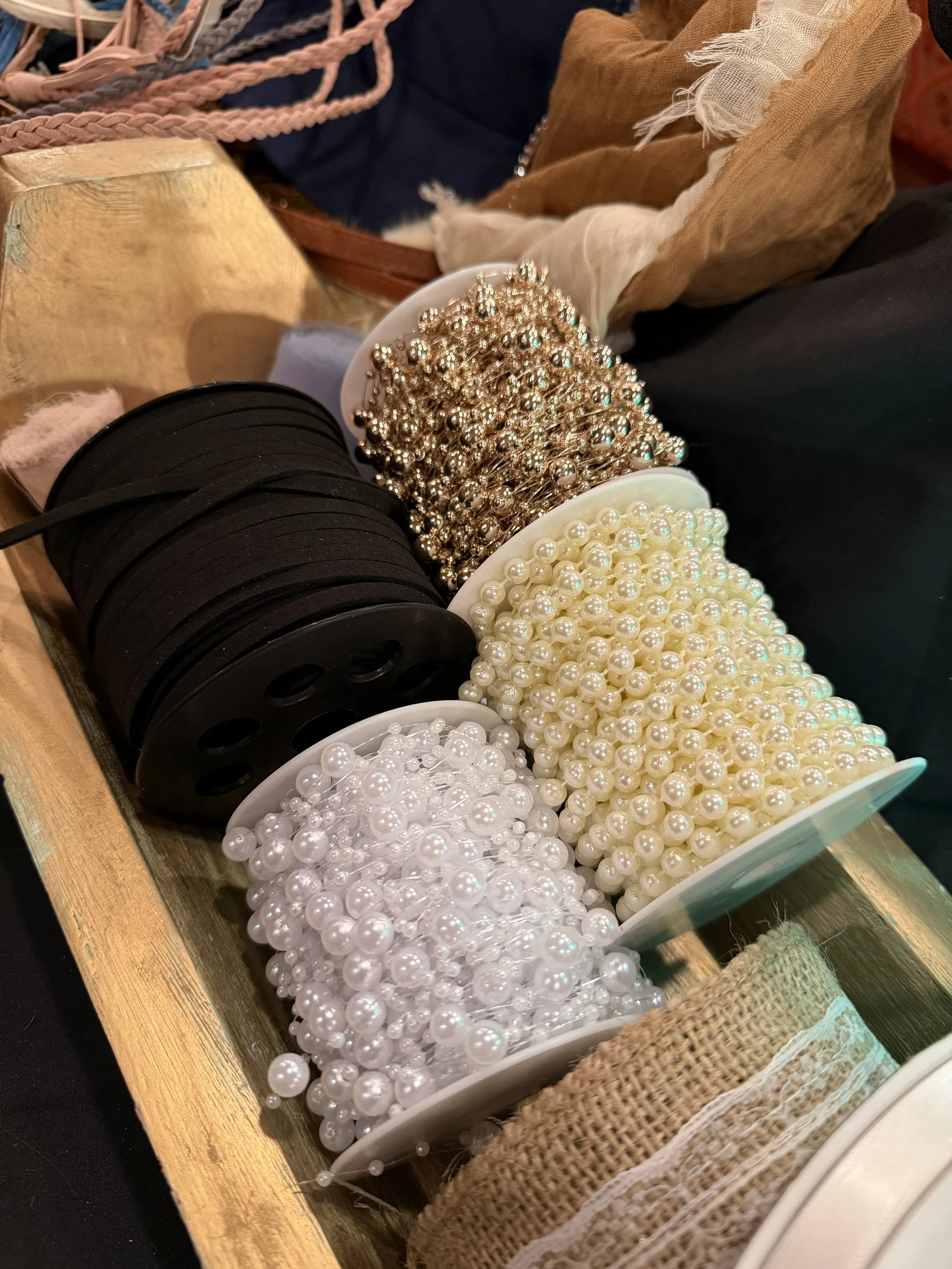 Assorted pearl and rhinestone jewelry and hair accessories in bowls on a wooden shelf.