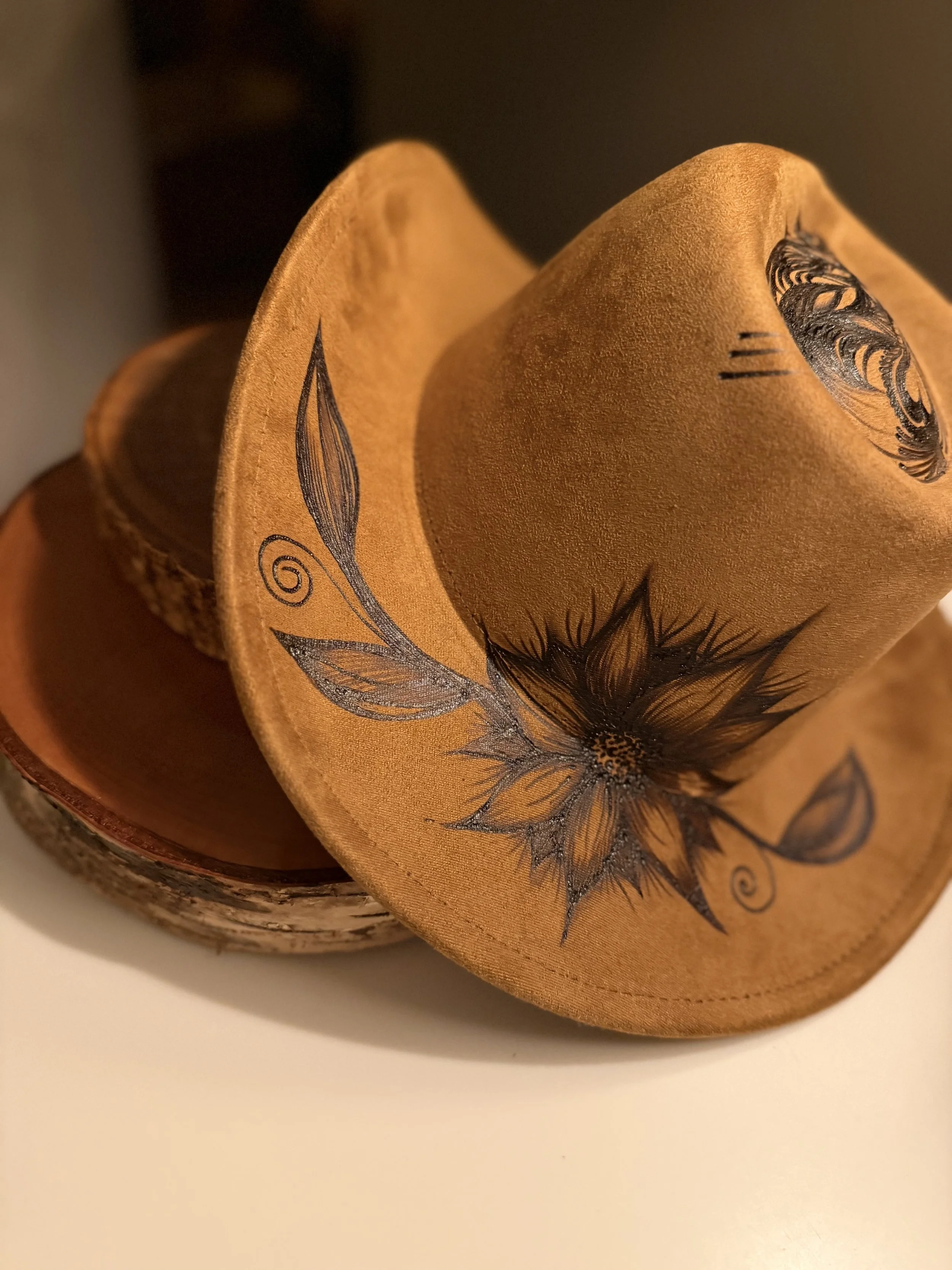 Close-up of a fabric item with a floral and feather design, partially covering a cup or container. The fabric is in shades of orange and includes black ink illustrations.