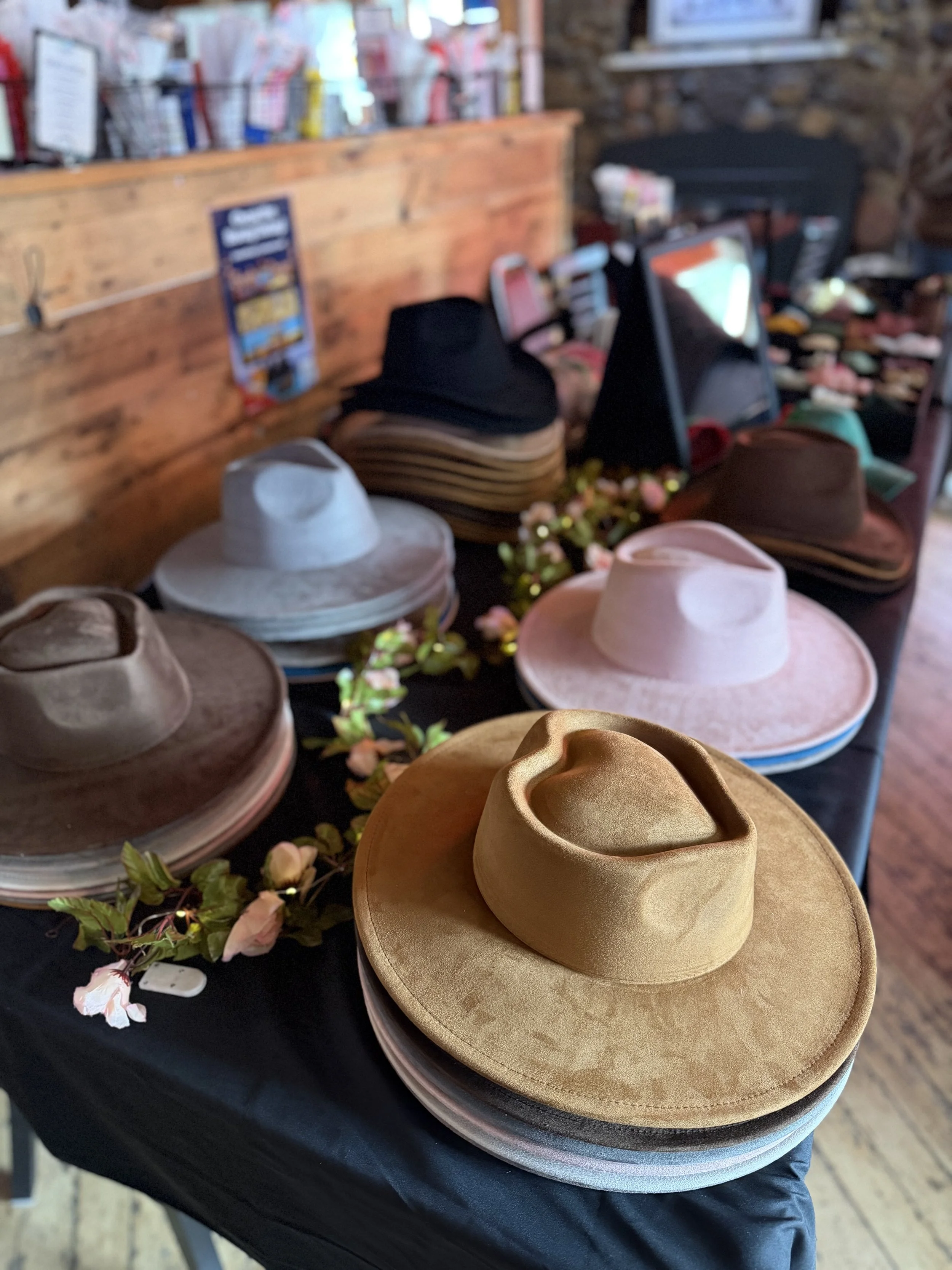 Several straw cowboy hats on display on a black table with flower decoration, in a rustic store setting.