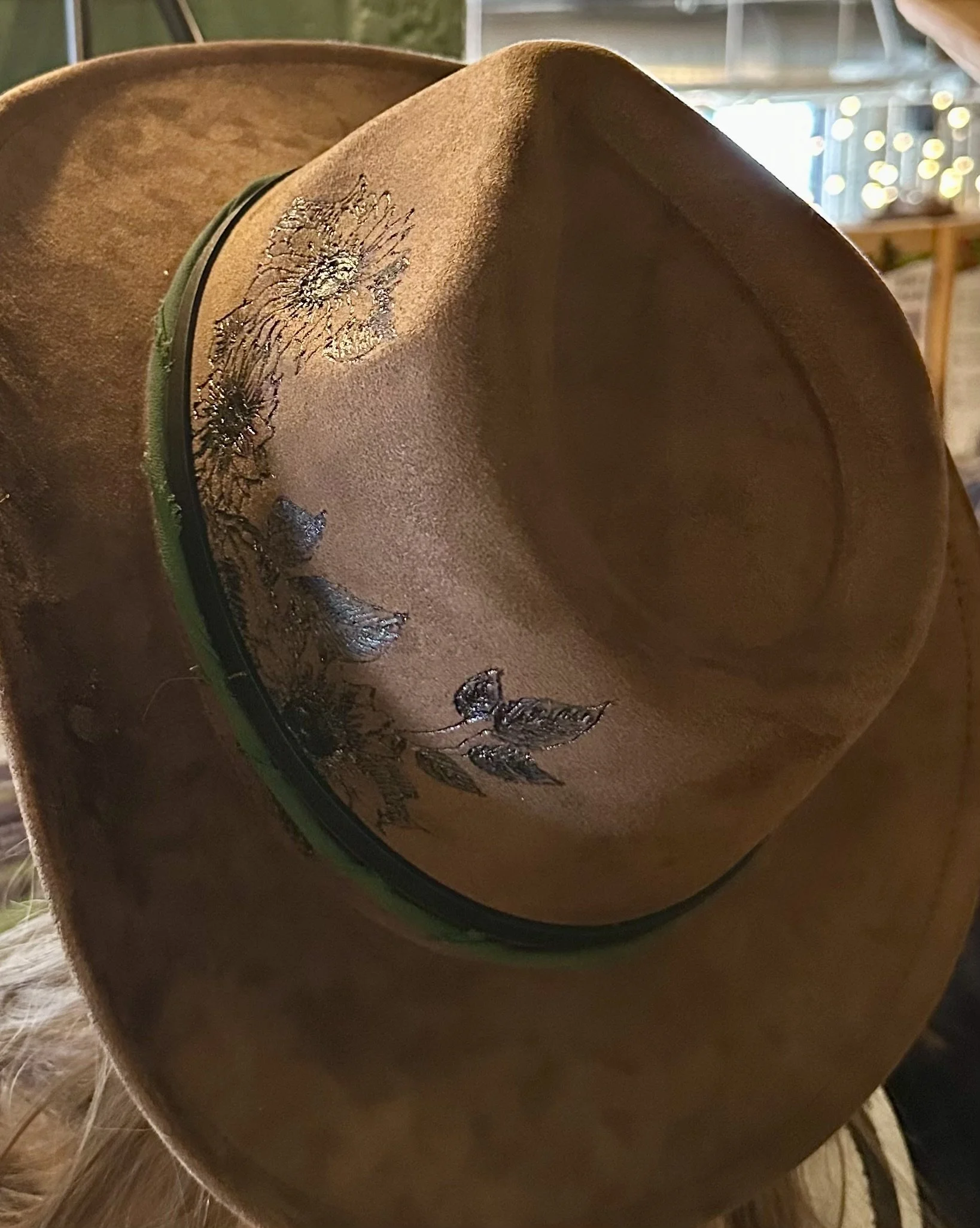Close-up of a cowboy hat with decorative feathers and a floral embroidery pattern on the band, placed on a wooden surface.