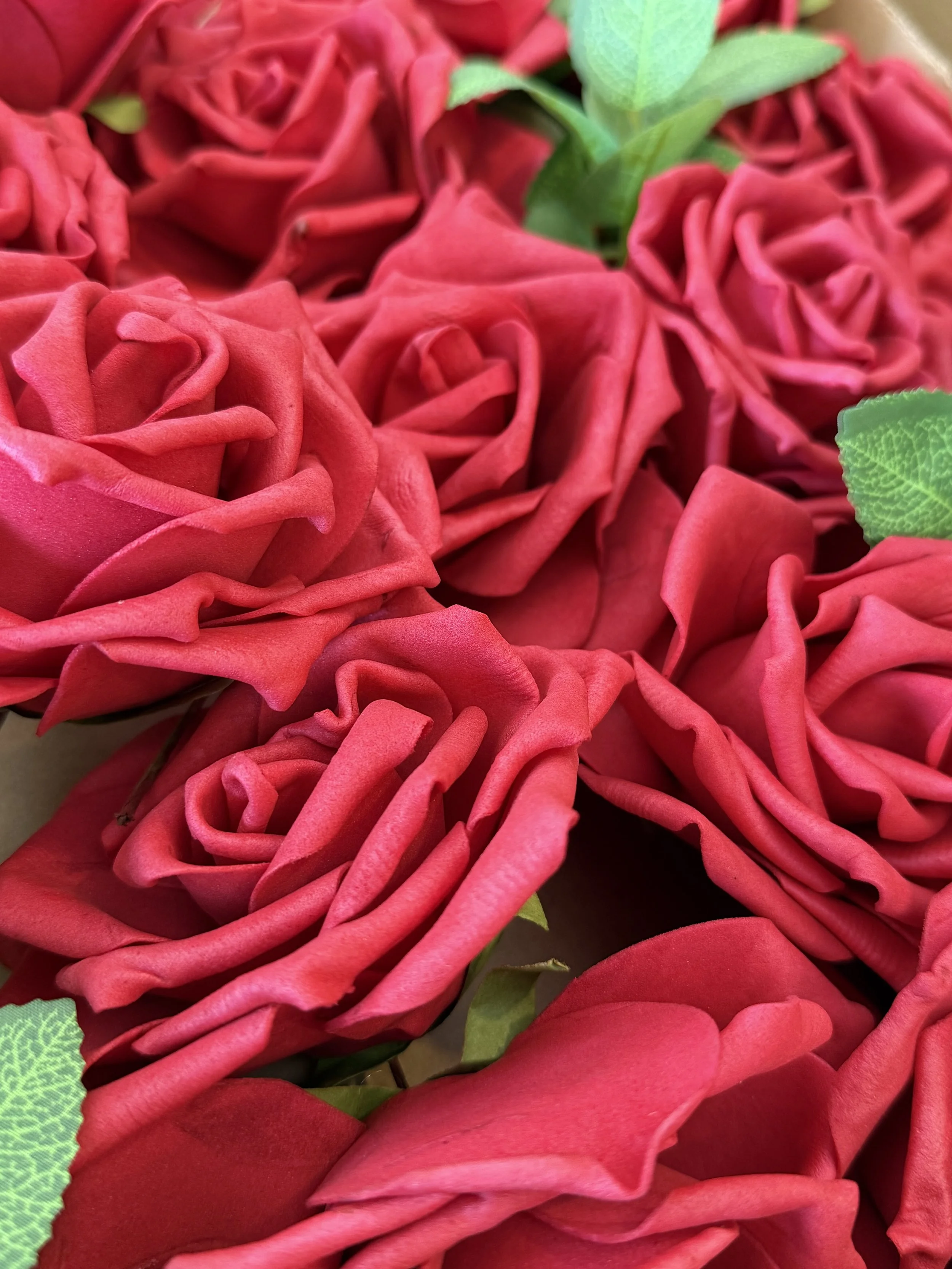 Close-up of red artificial roses with green leaves.