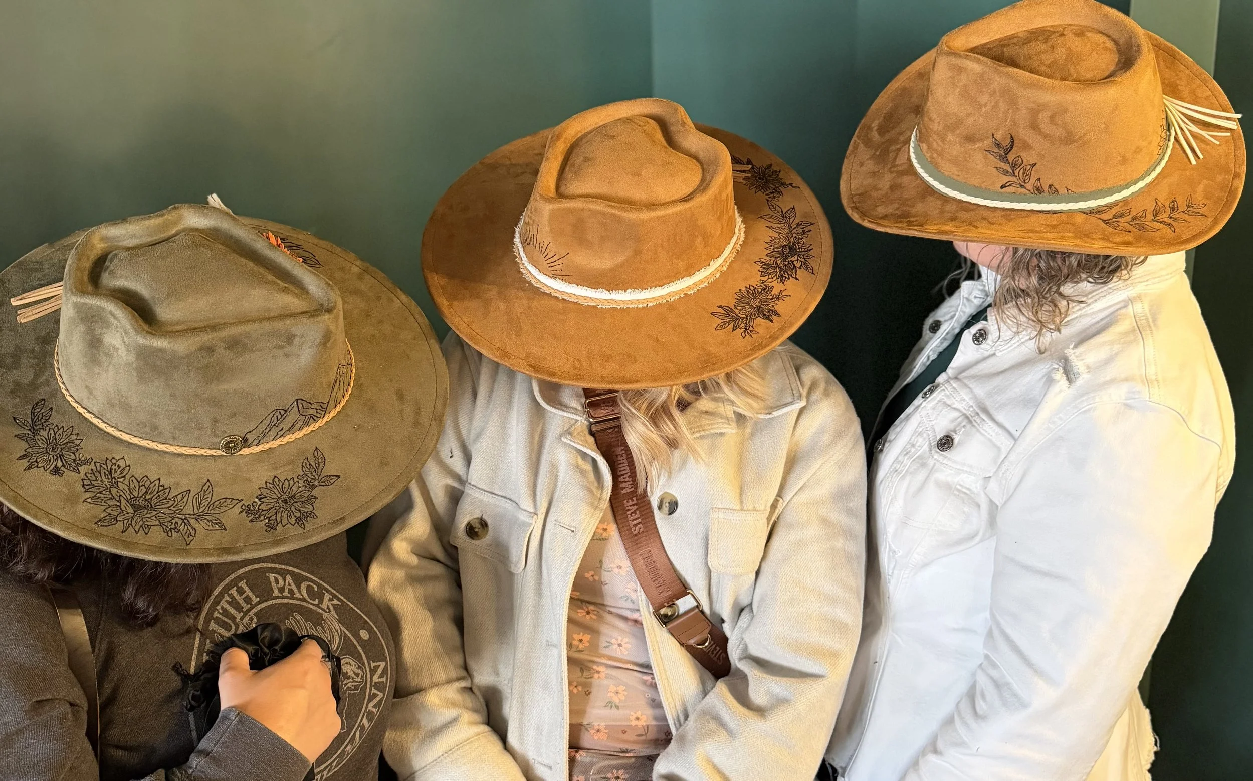 Three people wearing cowboy hats, two with embroidered floral designs, and one with a plain hat. Their faces are not visible as the photo is taken from above.