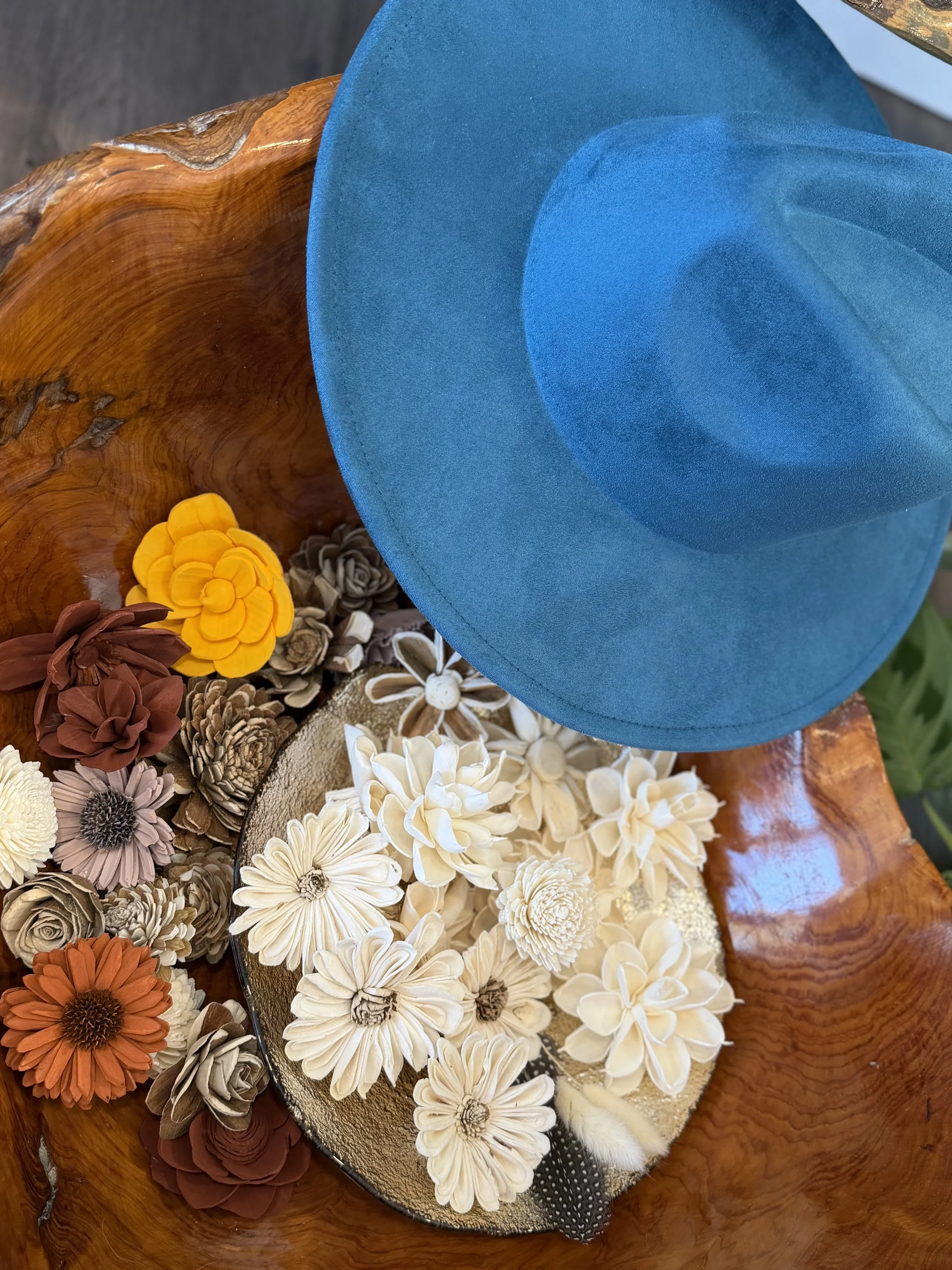 A collection of dried flowers and plants arranged on a table with a wooden surface, alongside a blue hat and a black container.