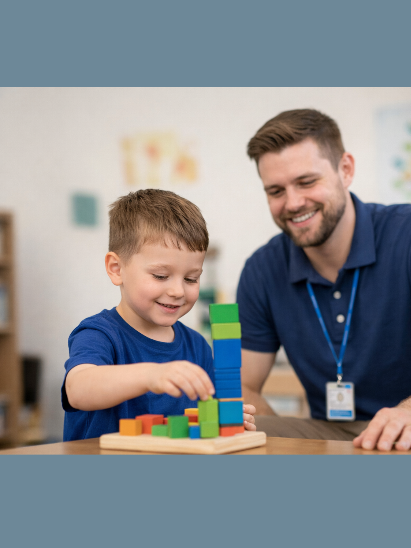 A young boy and an adult man, likely a teacher or therapist, playing with colorful wooden blocks at a table in a classroom setting.