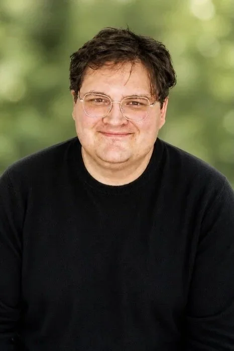 Male presenting figure, facing camera, and smiling.