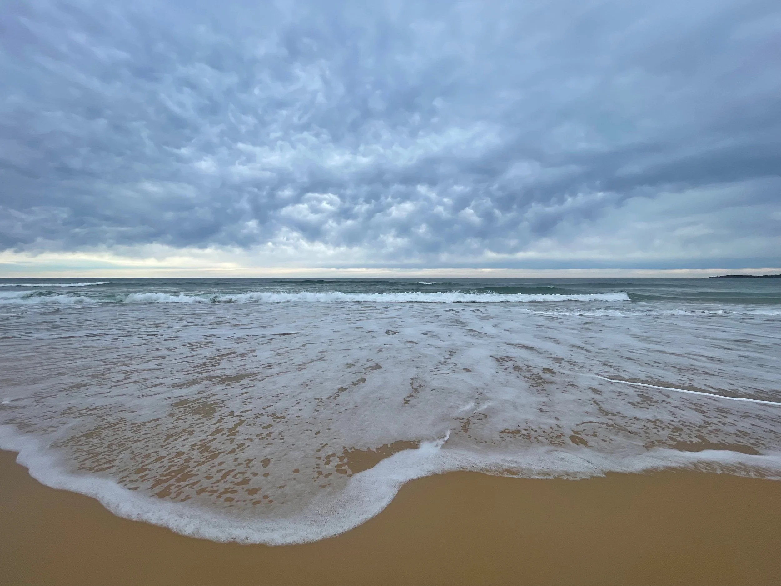 Empty sandy beach with gentle waves and a cloudy sky.