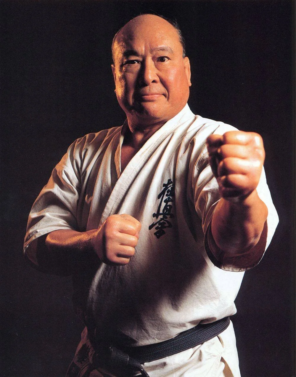 Sosai Mas Oyama, founder of Kyokushin, dressed in a karate gi with black belt, posing in a fighting stance with a fist extended toward the camera.