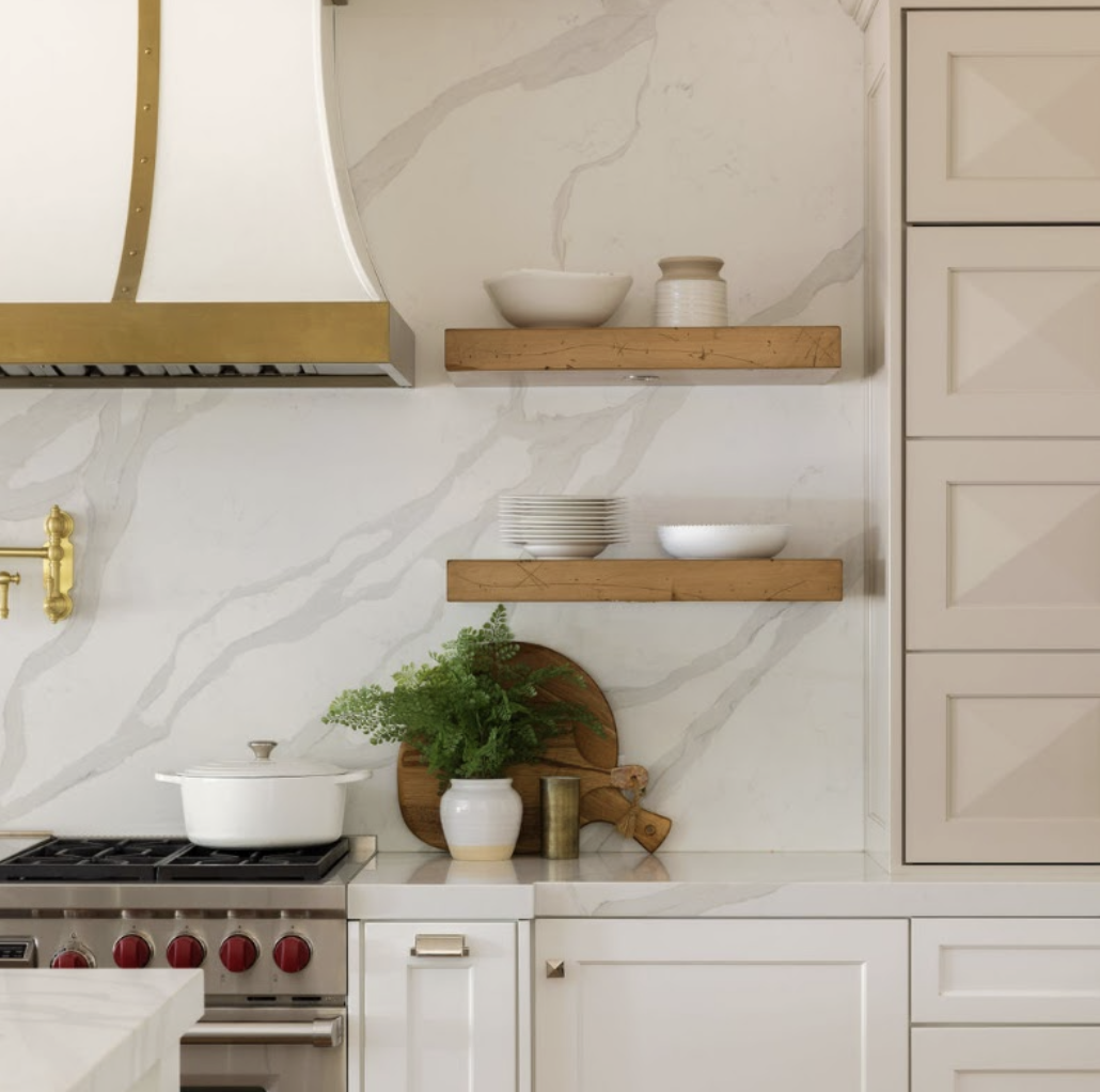 Kitchen with white cabinets, marble backsplash, open wooden shelves with bowls and jars, potted green plant on the counter, and a stove with red knobs.