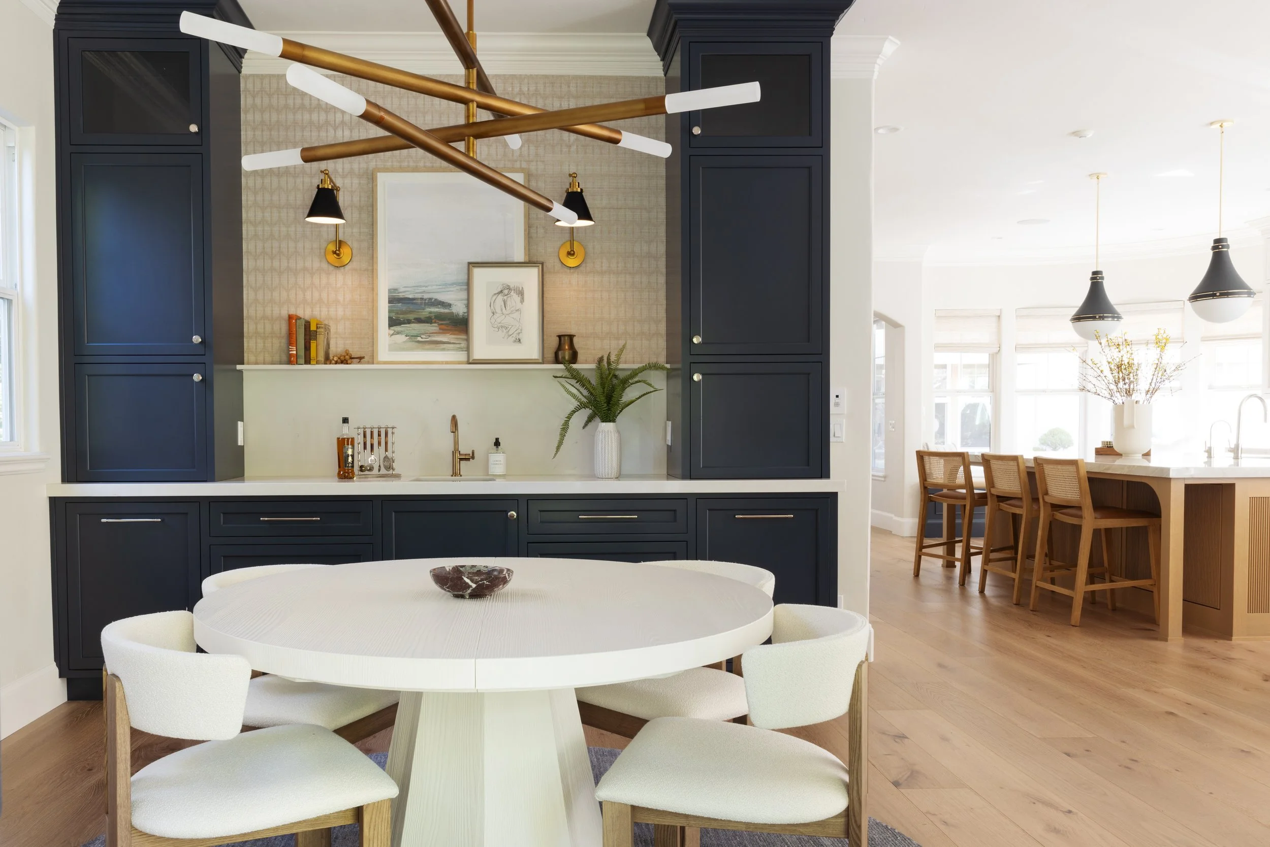 A modern kitchen with navy blue cabinets, a white round table surrounded by white chairs, and open concept kitchen and dining area with pendant lights and natural light.