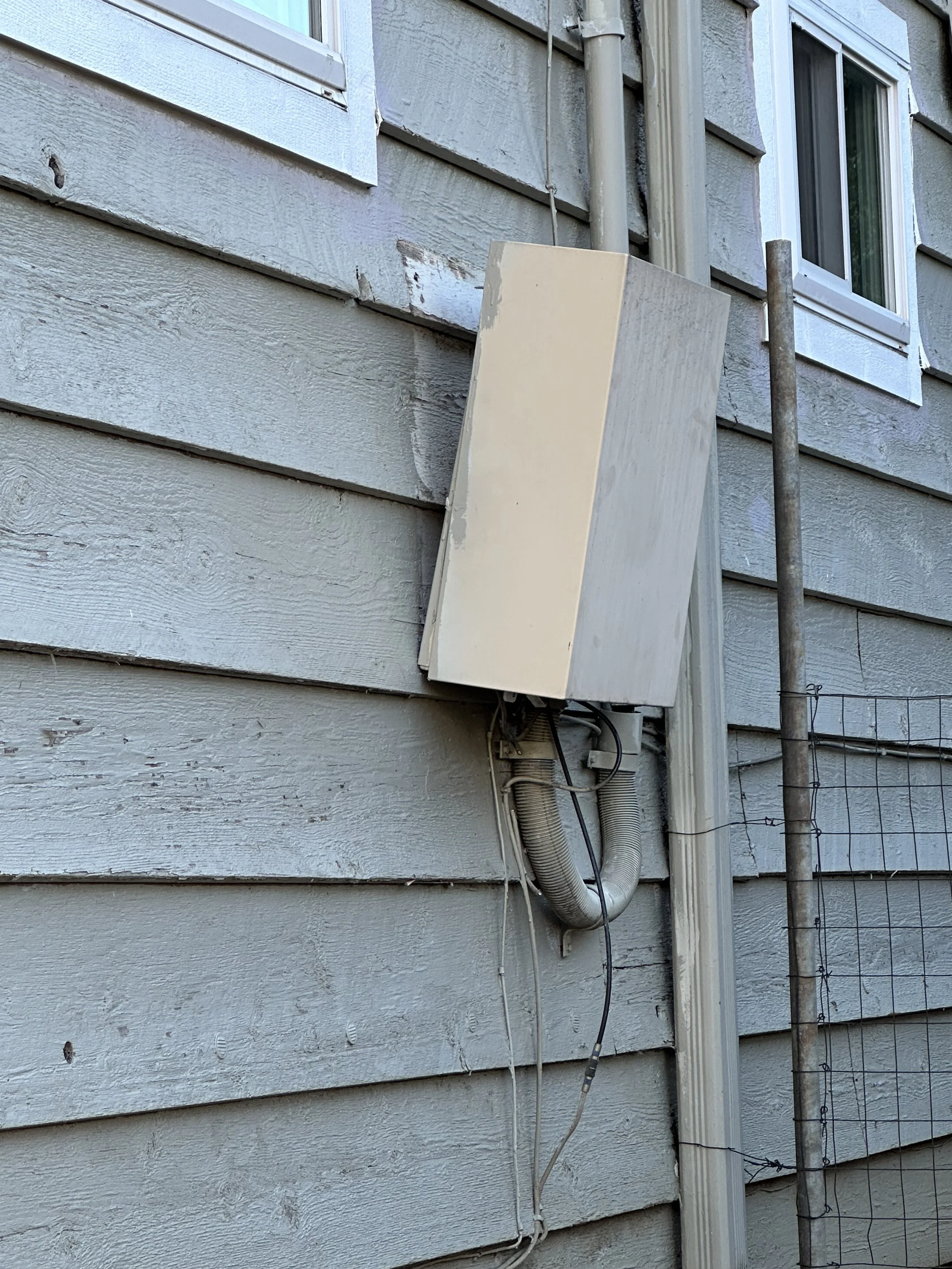 Close-up of a weathered house exterior with an electrical box, conduit pipes, and a window.