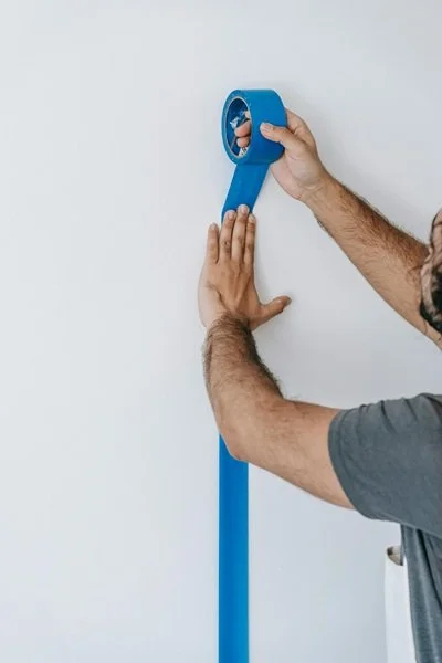 Man sticking blue tape to wall.