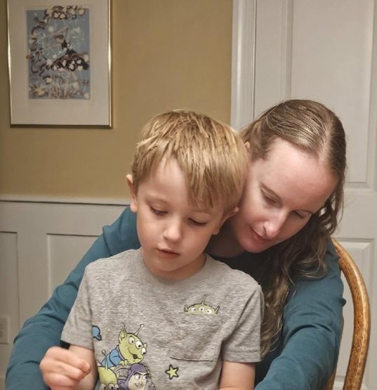 A woman and a young boy sitting closely together indoors, engaging in a shared activity.