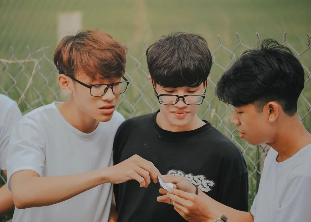 Three teen boys looking at something together.