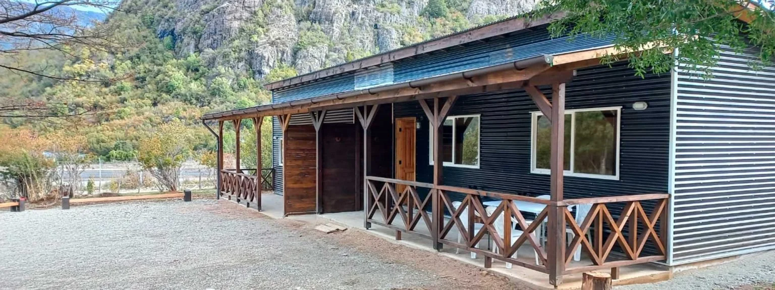 Casa de madera con terraza de balcón en un entorno natural con árboles y montañas.