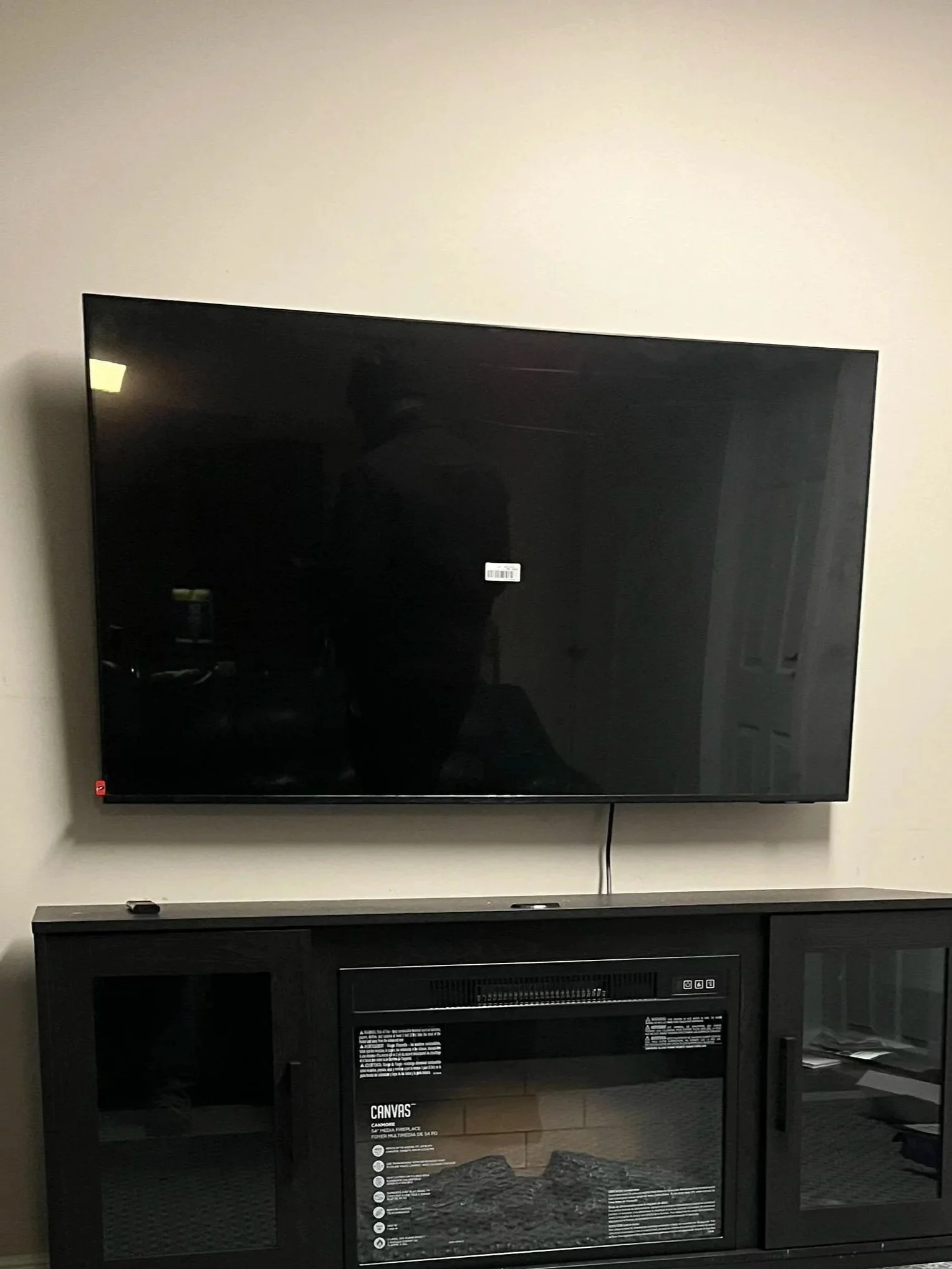 Flat-screen TV mounted on wall above a black media cabinet with a fireplace insert.