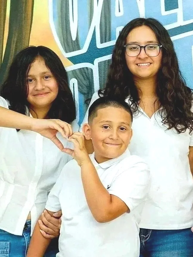 Group of seven children smiling and posing for the camera in front of a colorful background with the word "VALERIA" partially visible.