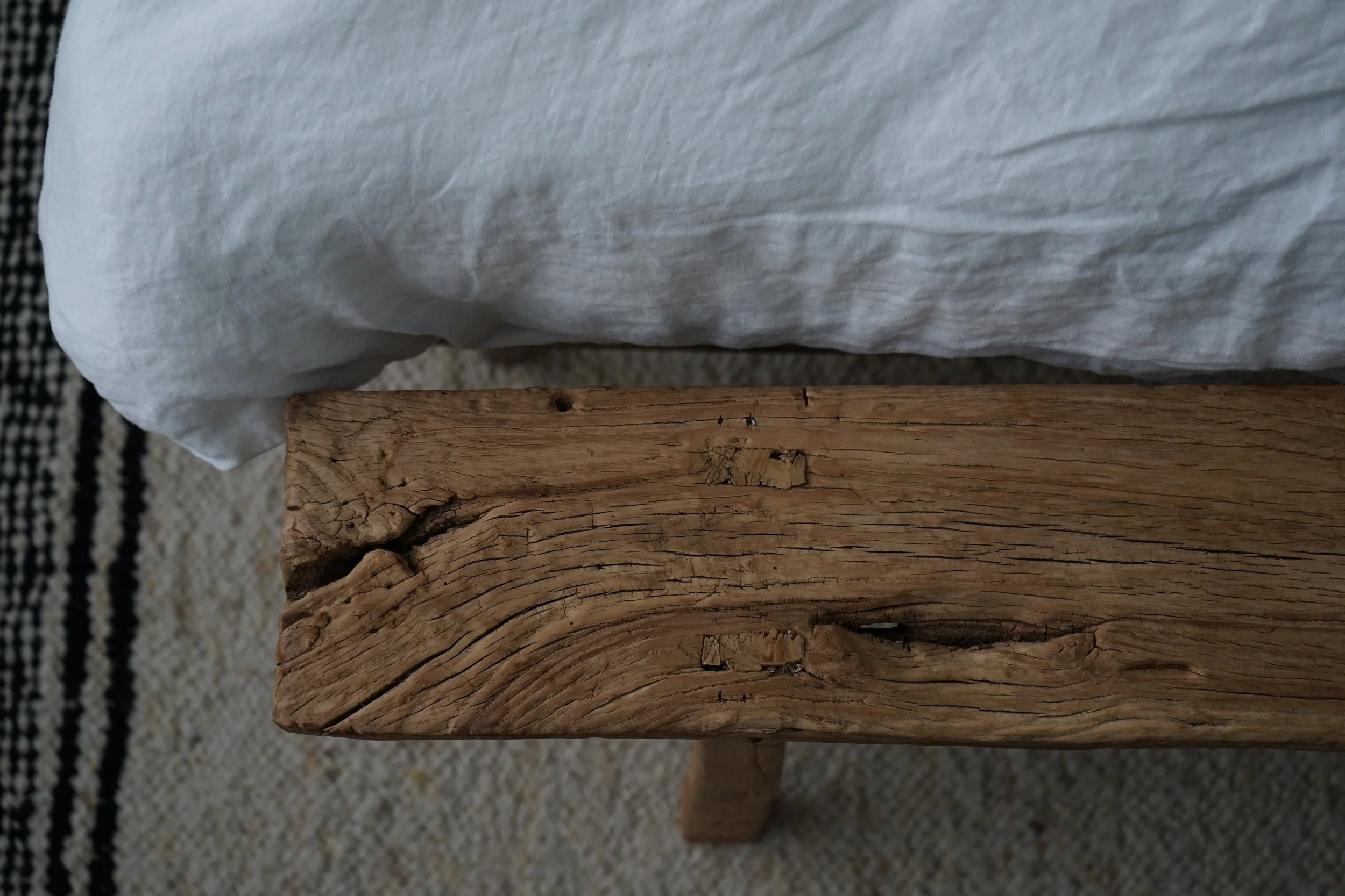 Close-up of a wooden bench with a white pillow resting on it, placed on a woven textured rug.