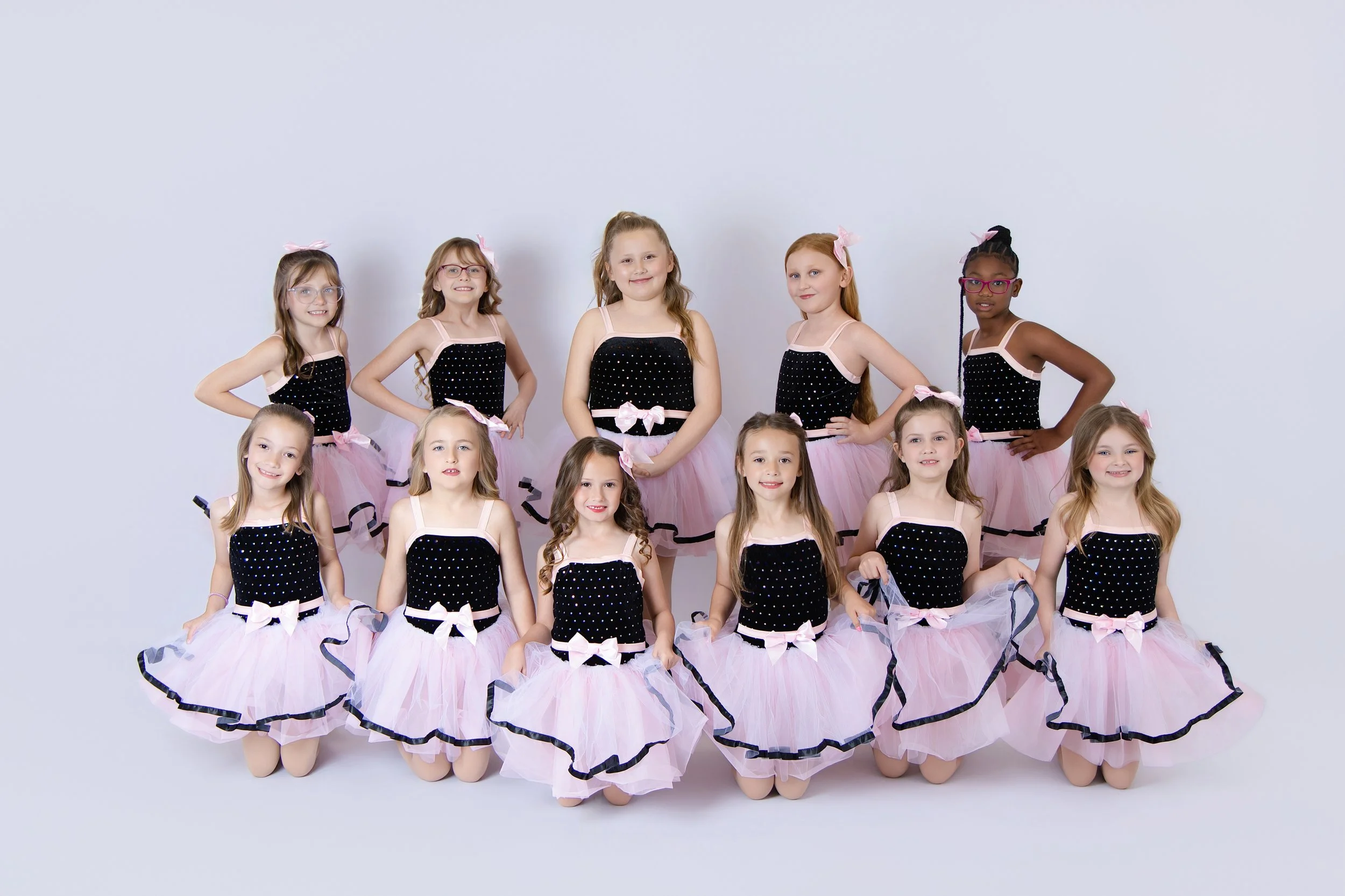 Group of young girls in dance costumes standing and kneeling against a plain white background
