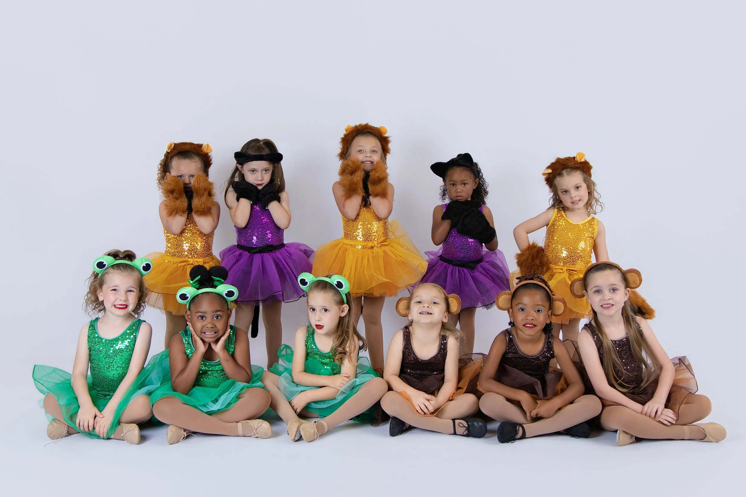 A group of young girls wearing colorful dance costumes and animal-themed headbands or hats, posing together against a plain white background.