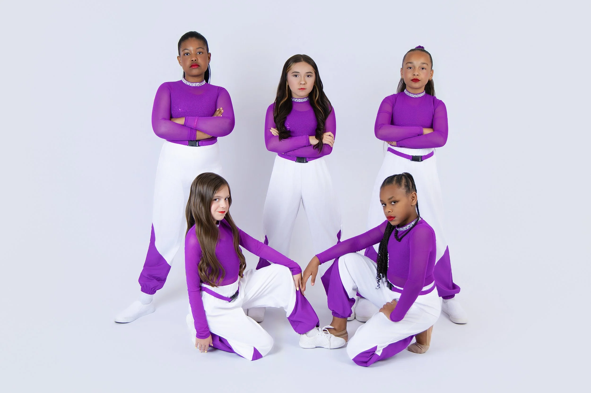 Six young girls dressed in coordinated purple and white dance costumes, posing against a plain white background.