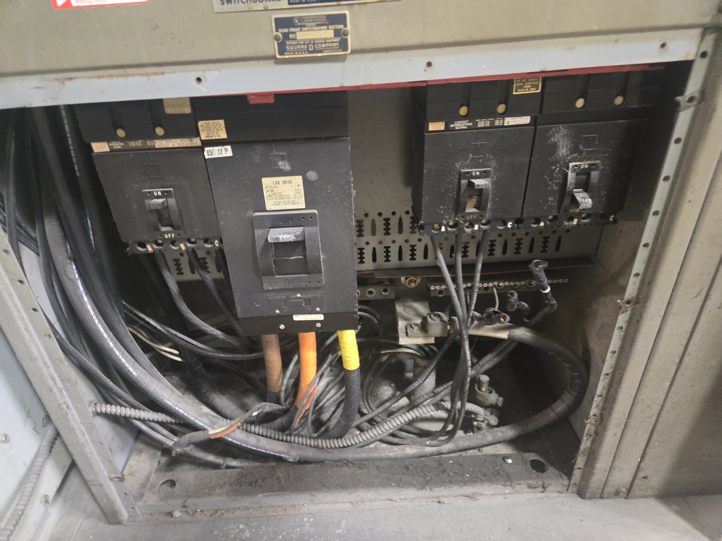 Electrical panel with circuit breakers, wires, and cables inside an open metal box.