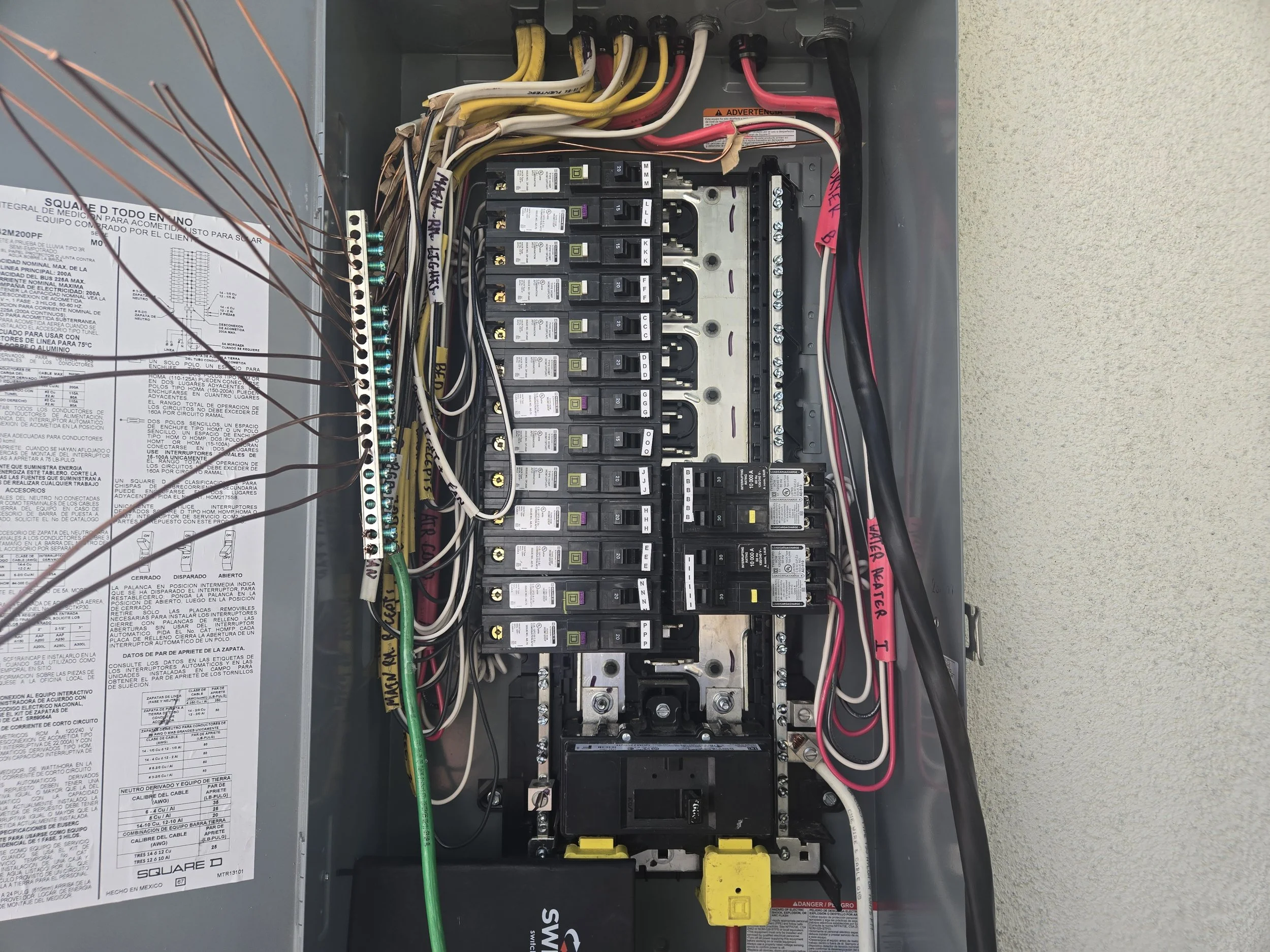 An electrical circuit breaker panel with multiple switches, wires, and labels, including a warning label on the side.