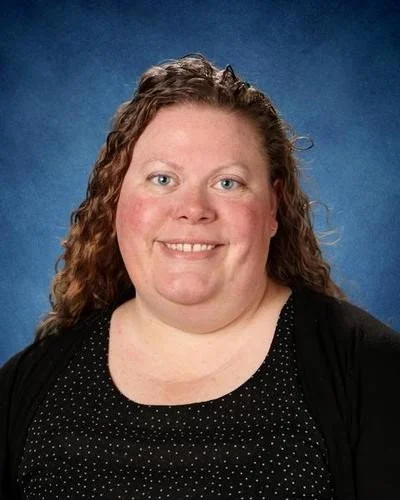 Portrait of a woman with curly hair smiling, wearing a black top with white dots against a blue background.