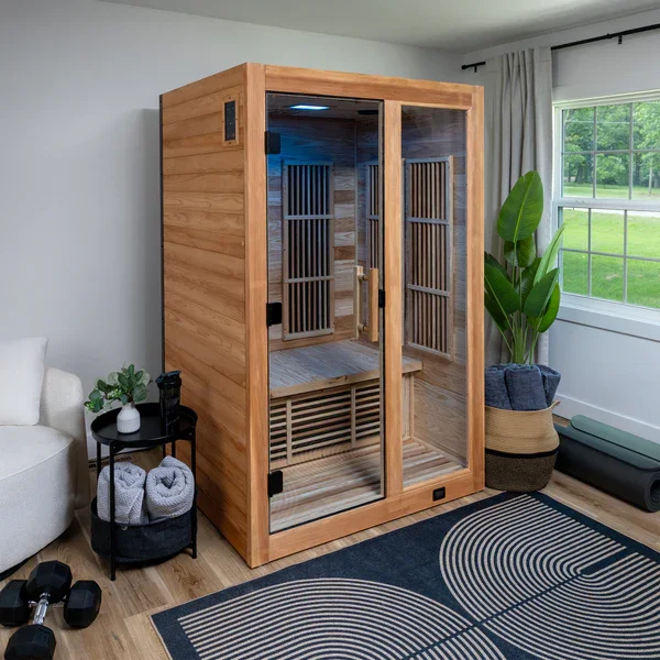 A wooden infrared sauna in a bright living room with a large window and green plants.