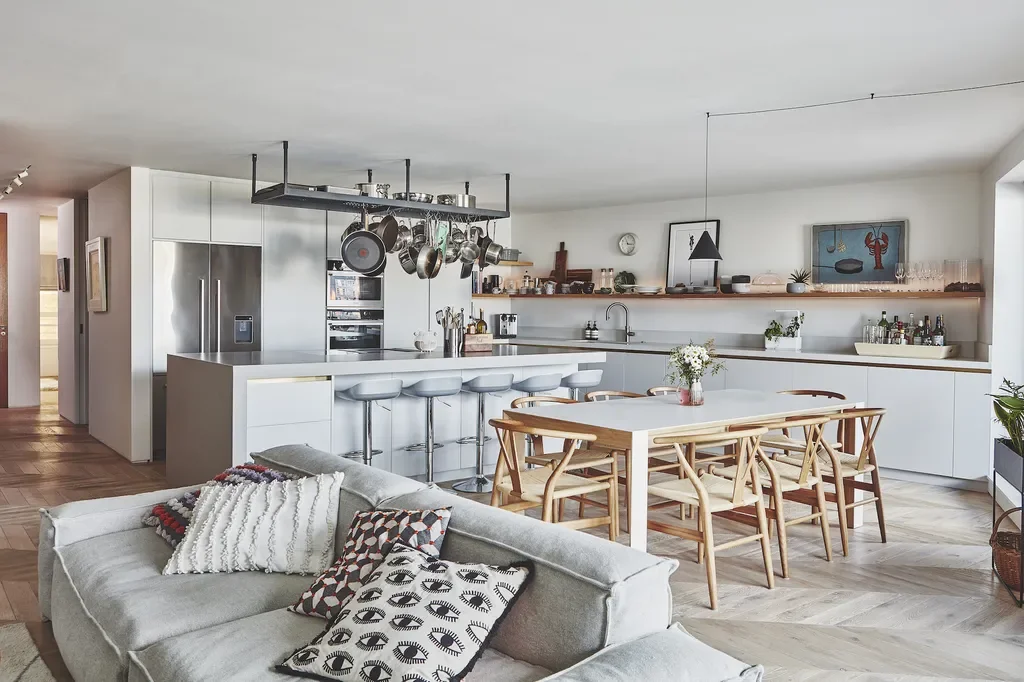 Open-concept kitchen and living space with a dining table, bar stools, and a grey sofa with decorative pillows.