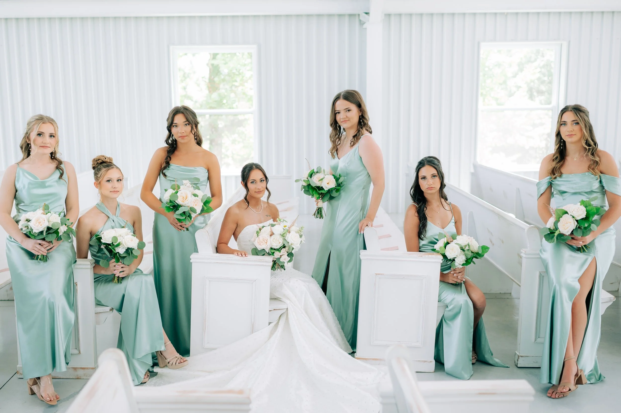 Bridals and bridesmaids in mint green dresses holding bouquets in a bright indoor setting with white walls and windows