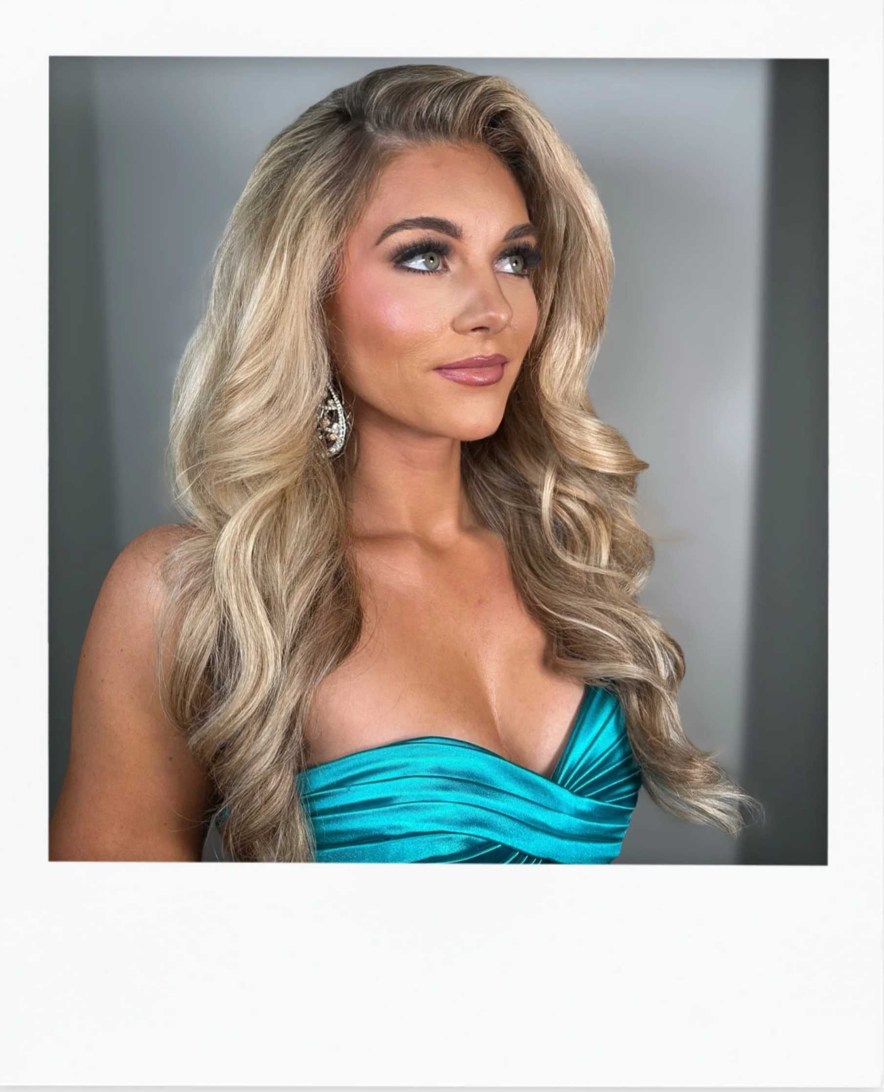 A woman with long, wavy blonde hair wearing a strapless turquoise dress and silver earrings.