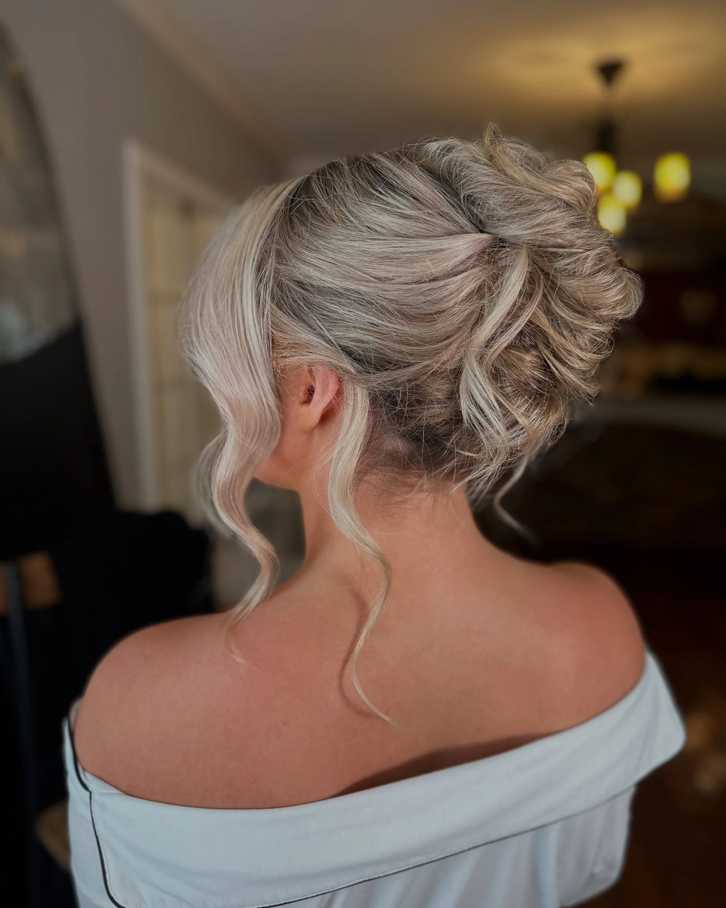 Back of a woman's head with styled silver hair in loose curls and waves, wearing an off-the-shoulder white top.