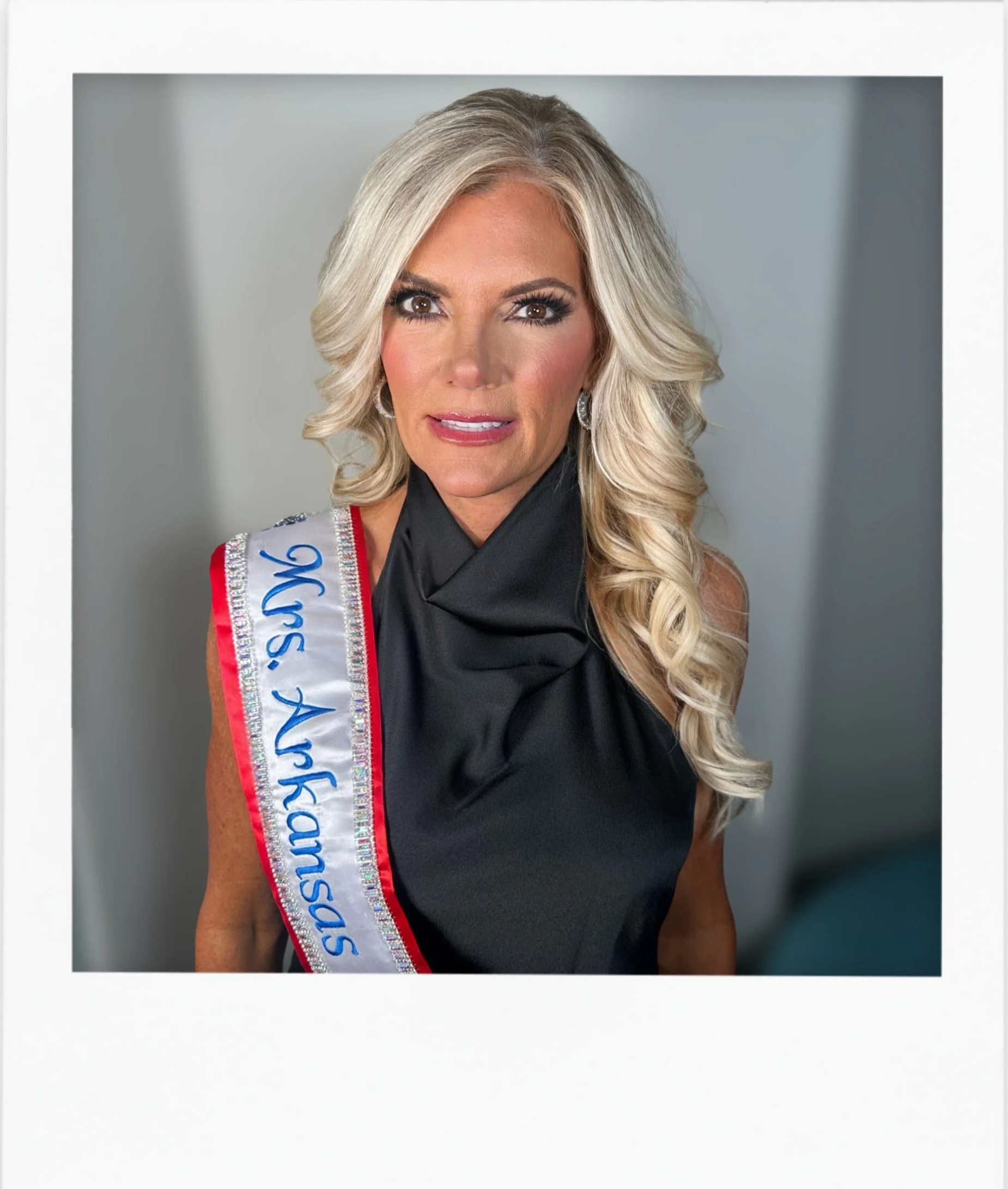 A woman with long blonde hair and makeup, wearing a black dress and earrings, with a sash that reads 'Ms. Texas USA'.