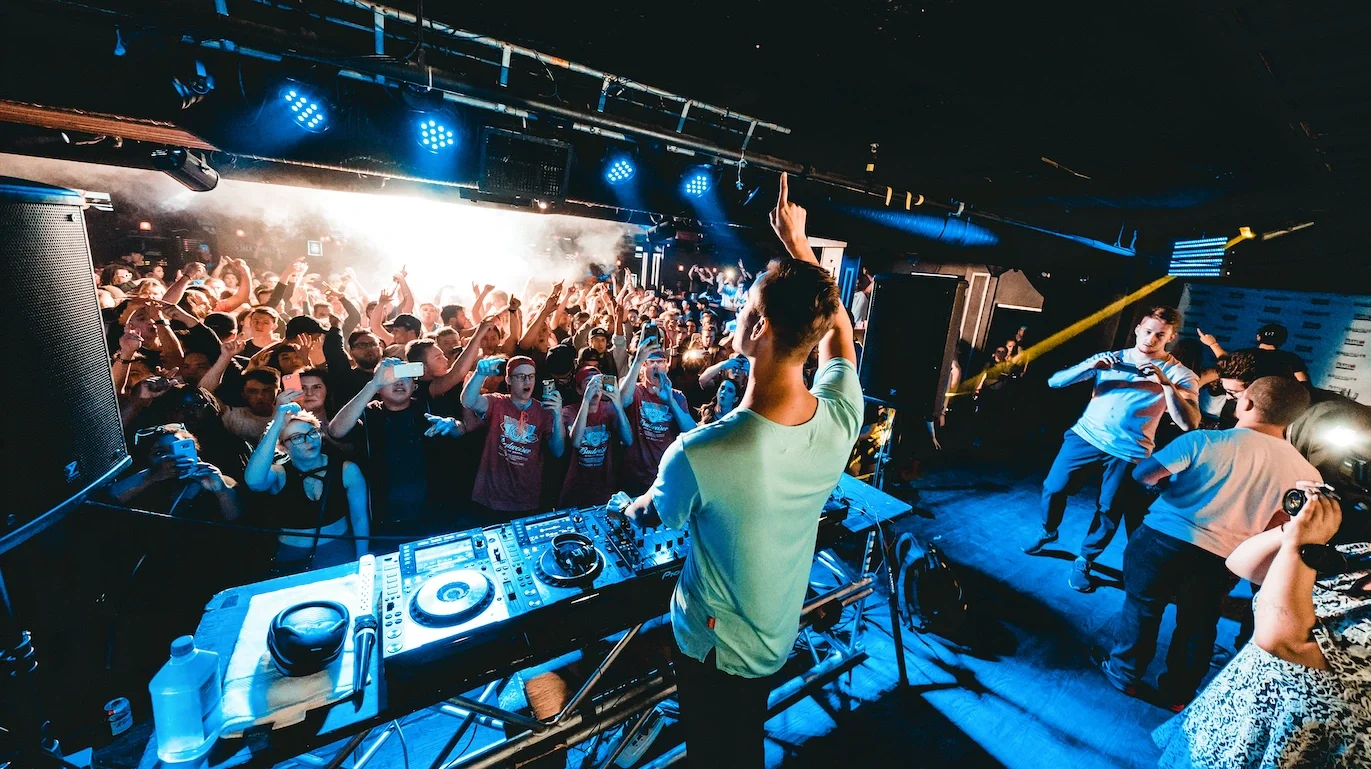 DJ performing on stage with crowd dancing and taking photos at a nightclub or concert venue