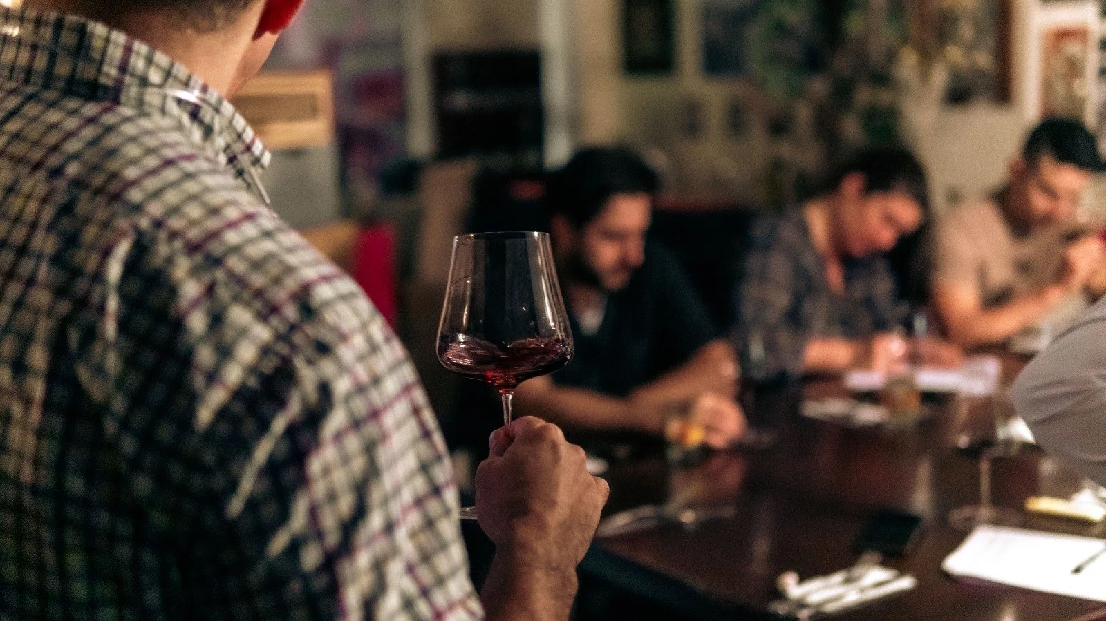 Persona sosteniendo una copa de vino tinto en una reunión social en un ambiente íntimo y acogedor