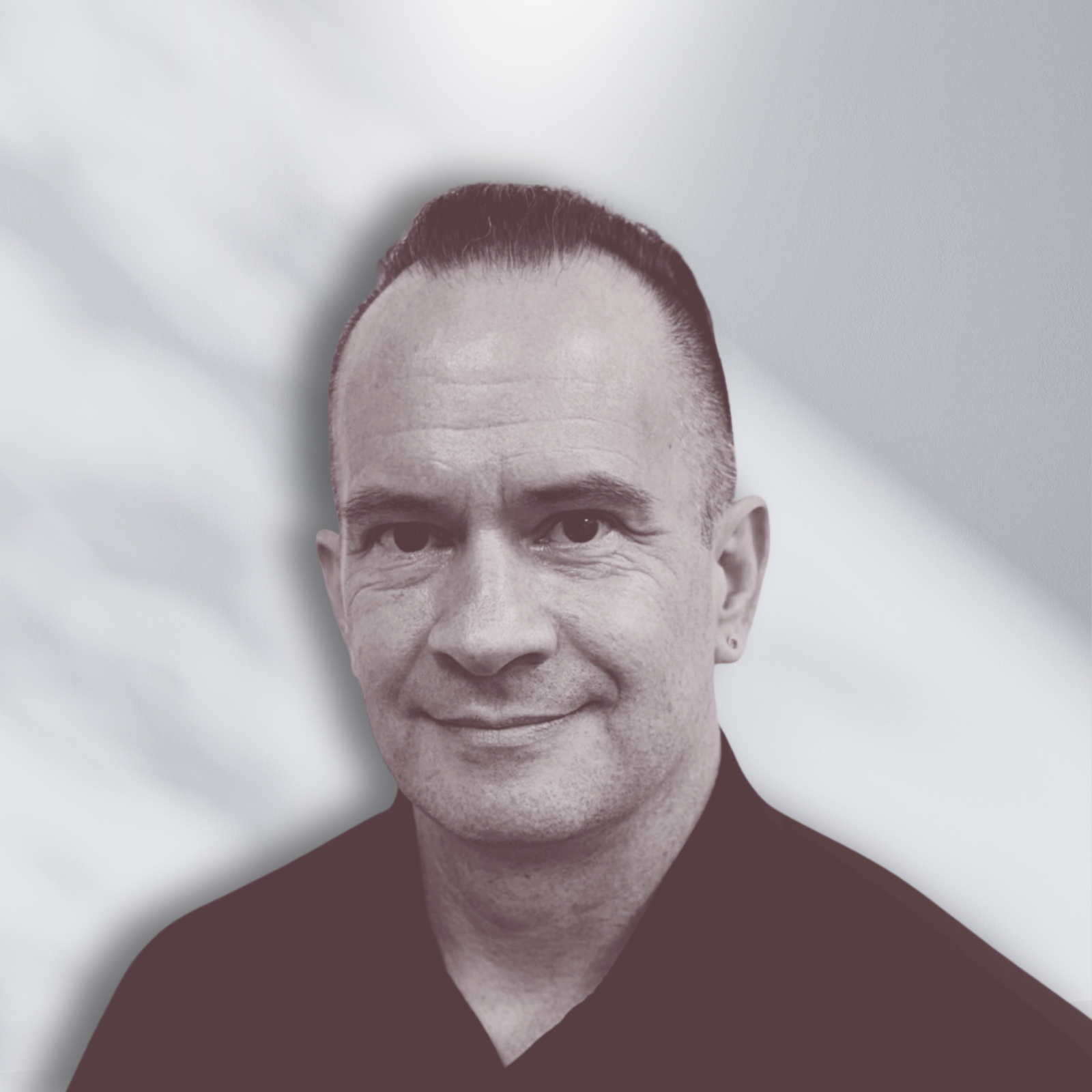 A black and white portrait of a smiling man with short dark hair, wearing a dark shirt, against a plain background.
