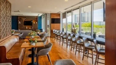 Interior of a modern restaurant with wooden floors, tables set with flowers, and large windows letting in natural light.