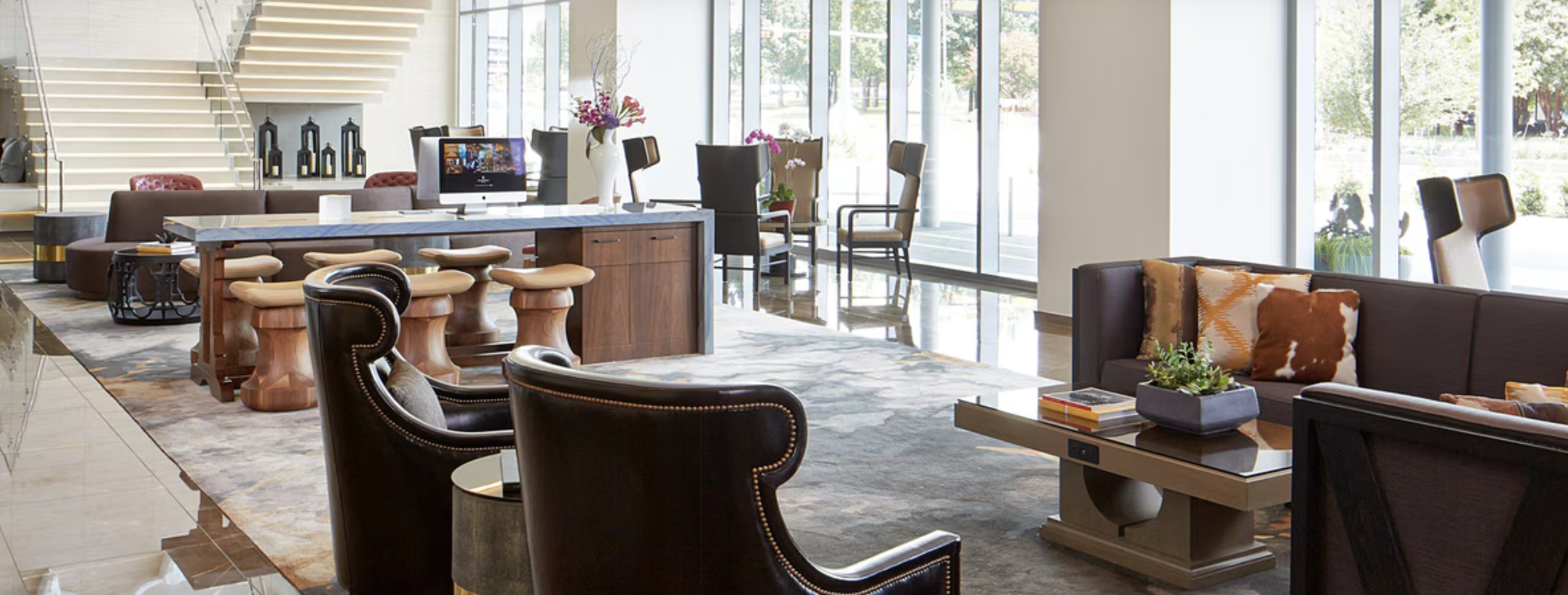 Modern hotel lobby with seating area, large windows, and decorative plants.